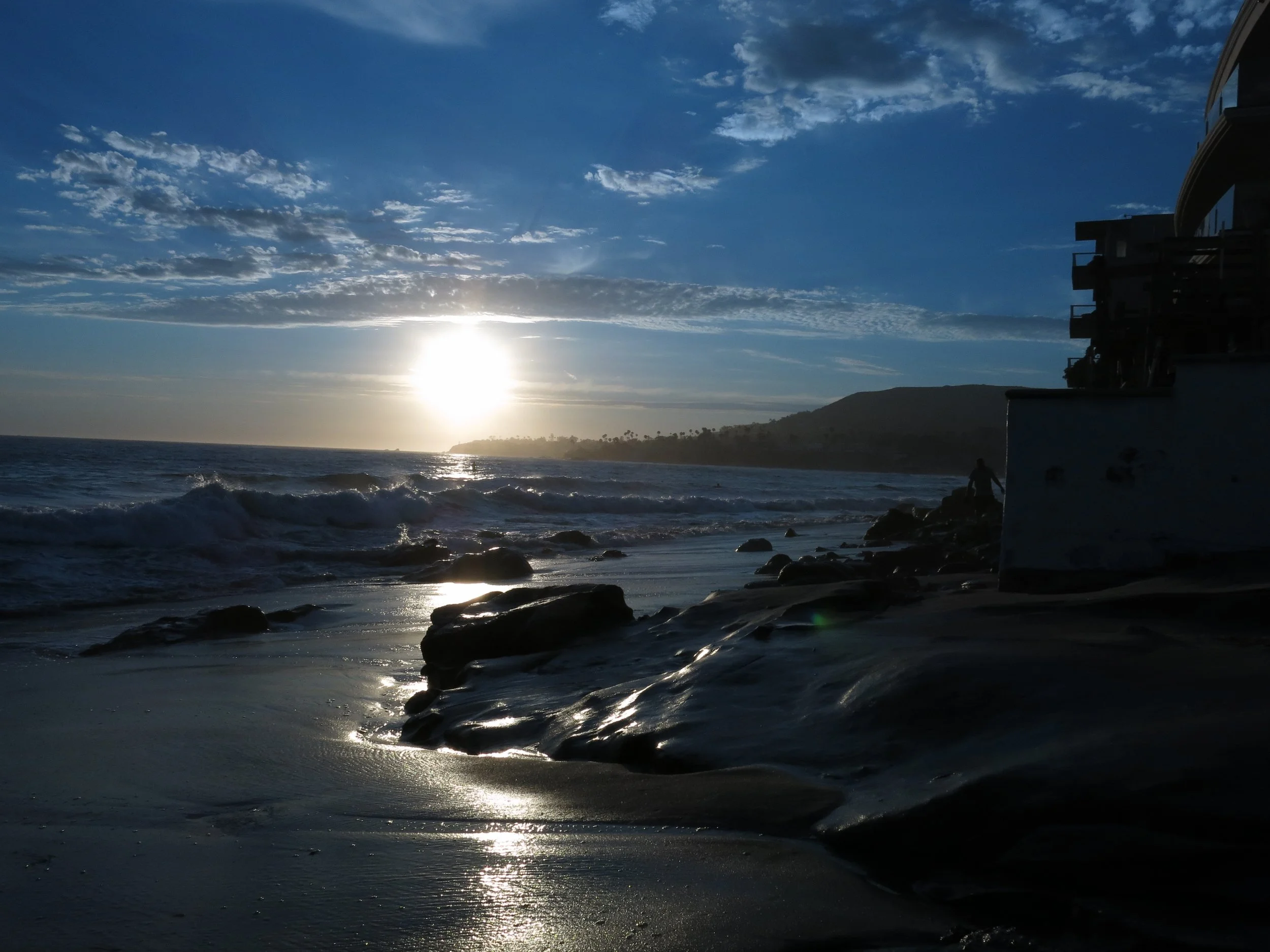 An image of a bright sun setting in a darkening sky sending a hope-filled trail of light across dark sand and rocks