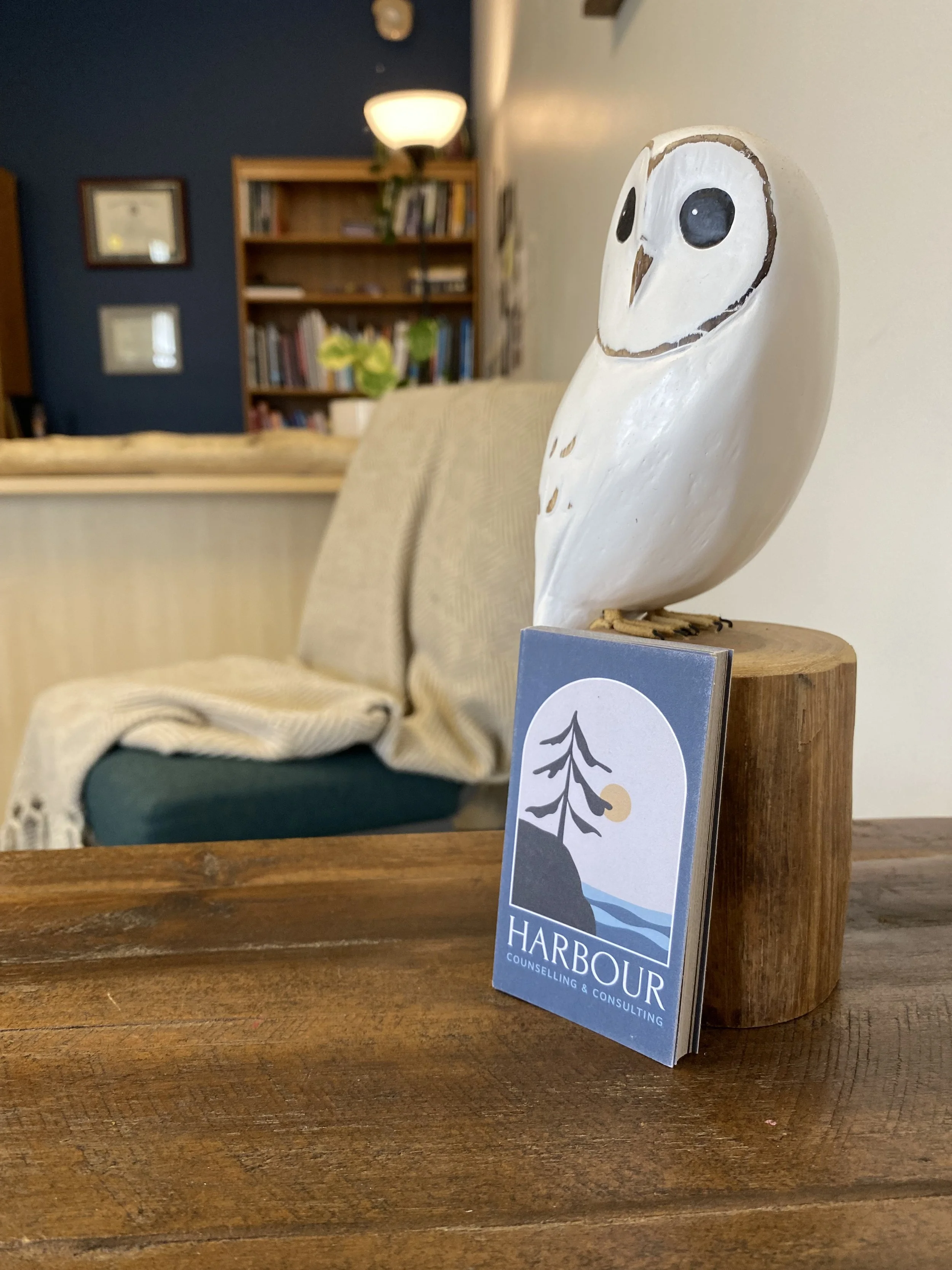 Our coastal-vibe business cards leaning against a wooden owl carving on the side table of our cozy counselling office in Surrey BC