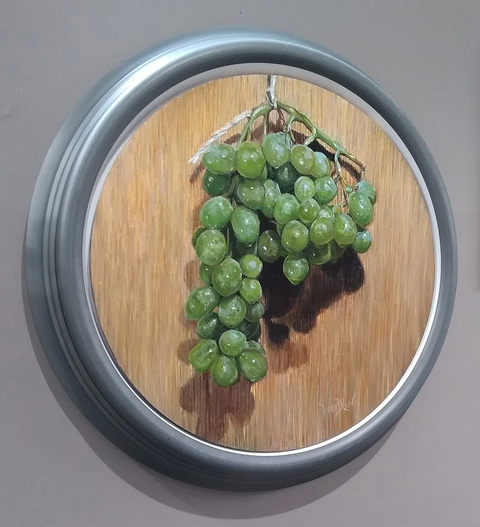 available oil painting of a cluster of green grapes hanging against a wooden backdrop in a circular frame