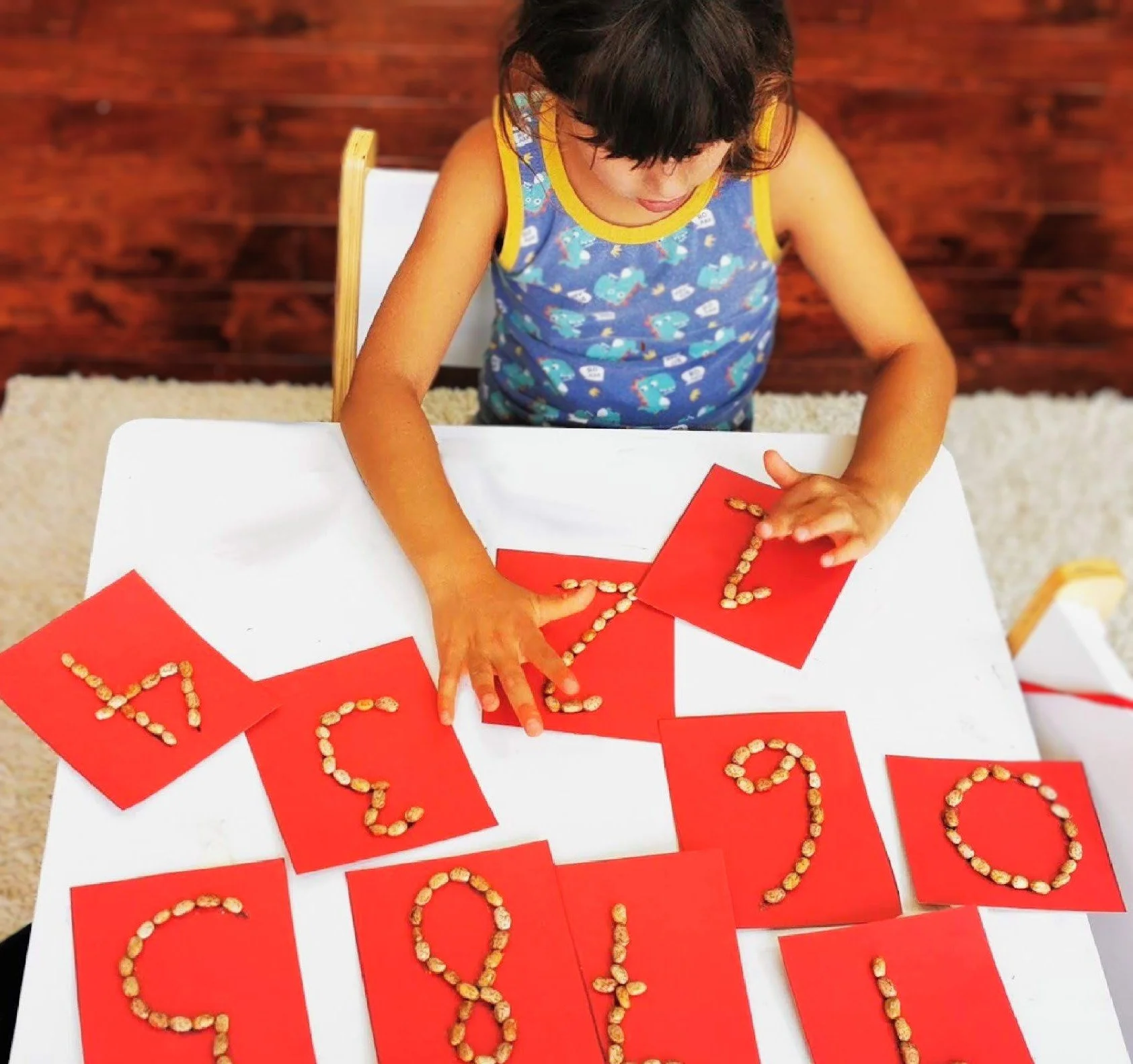 Child tracing sensory number cards with beans to support tactile learning, number recognition, and early math skills