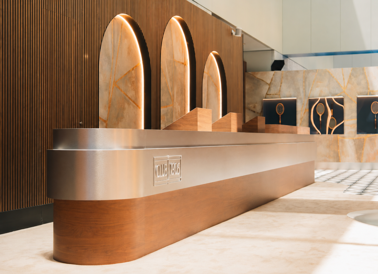 Modern reception desk with a wooden and metallic finish, illuminated decorative arch panels behind, and a marble wall with geometric gold accents.