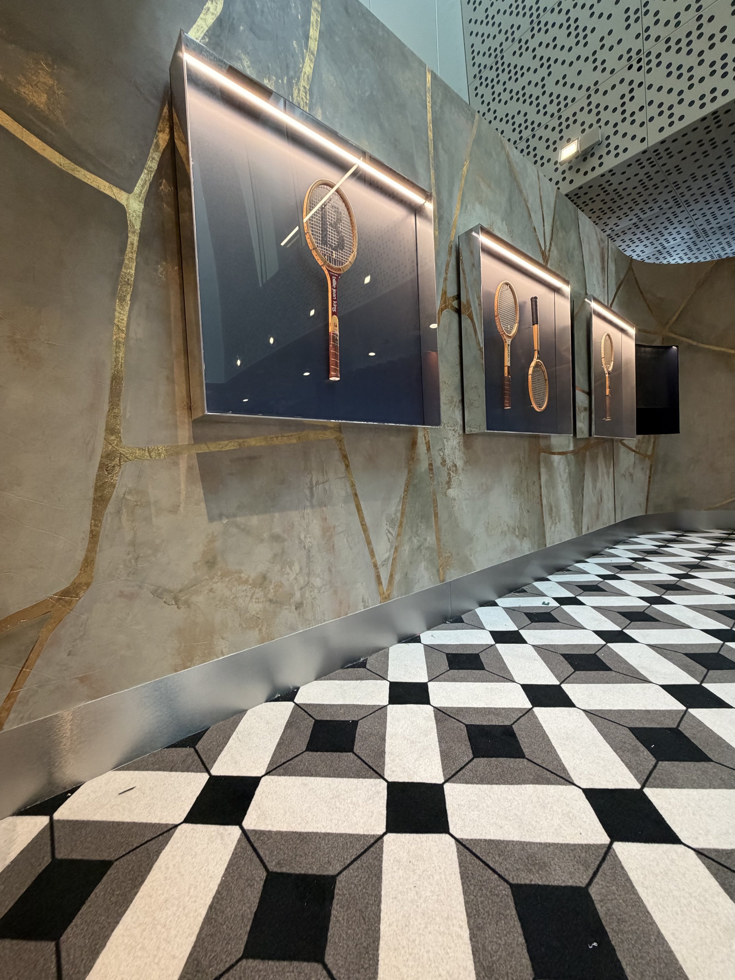 Tennis rackets framed on a wall display in a modern interior setting with black, white, and gray patterned floor tiles.