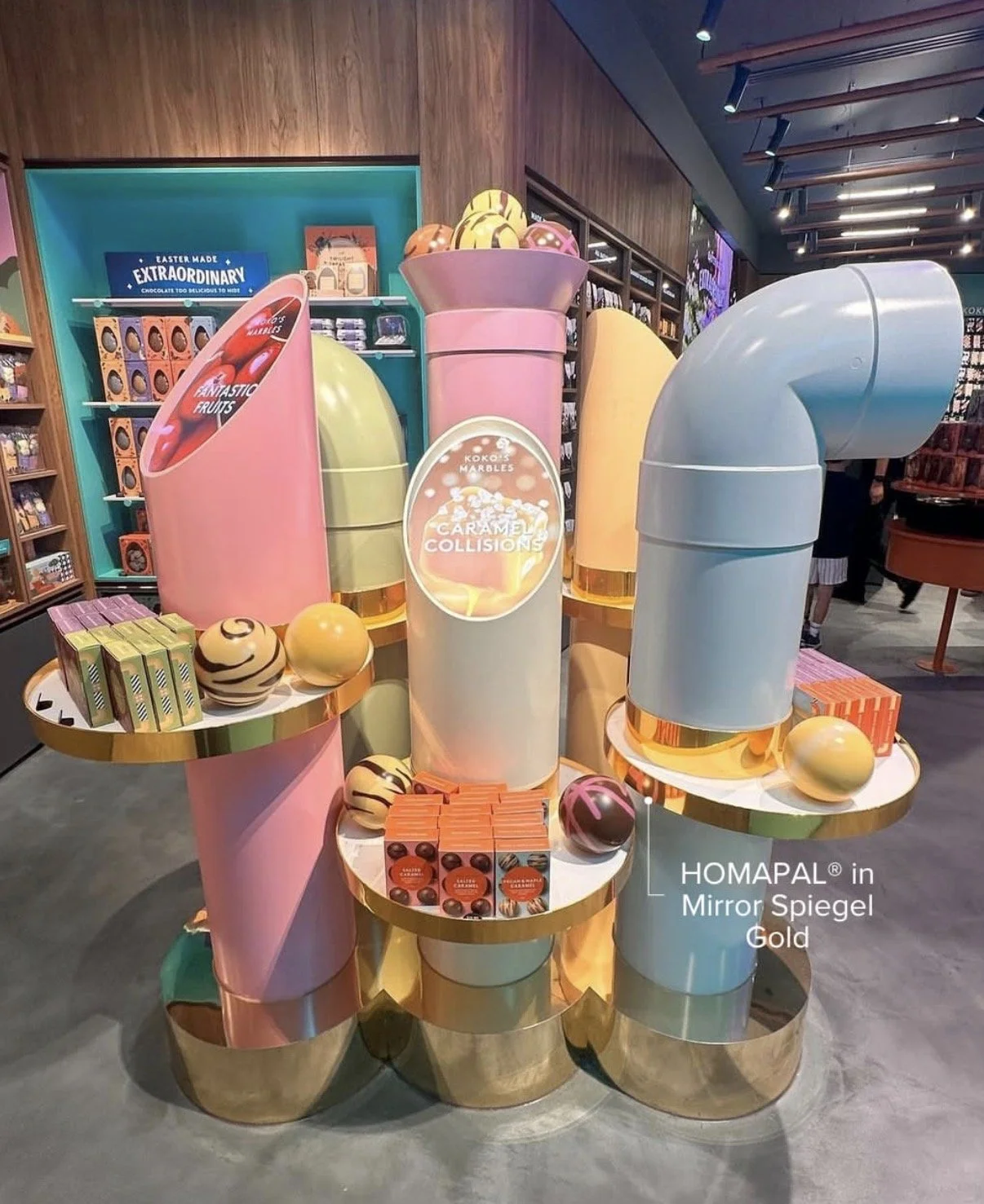 Colorful candy display shaped like giant tubes and spheres, with chocolate boxes and balls placed on a gold mirrored table in a candy store.