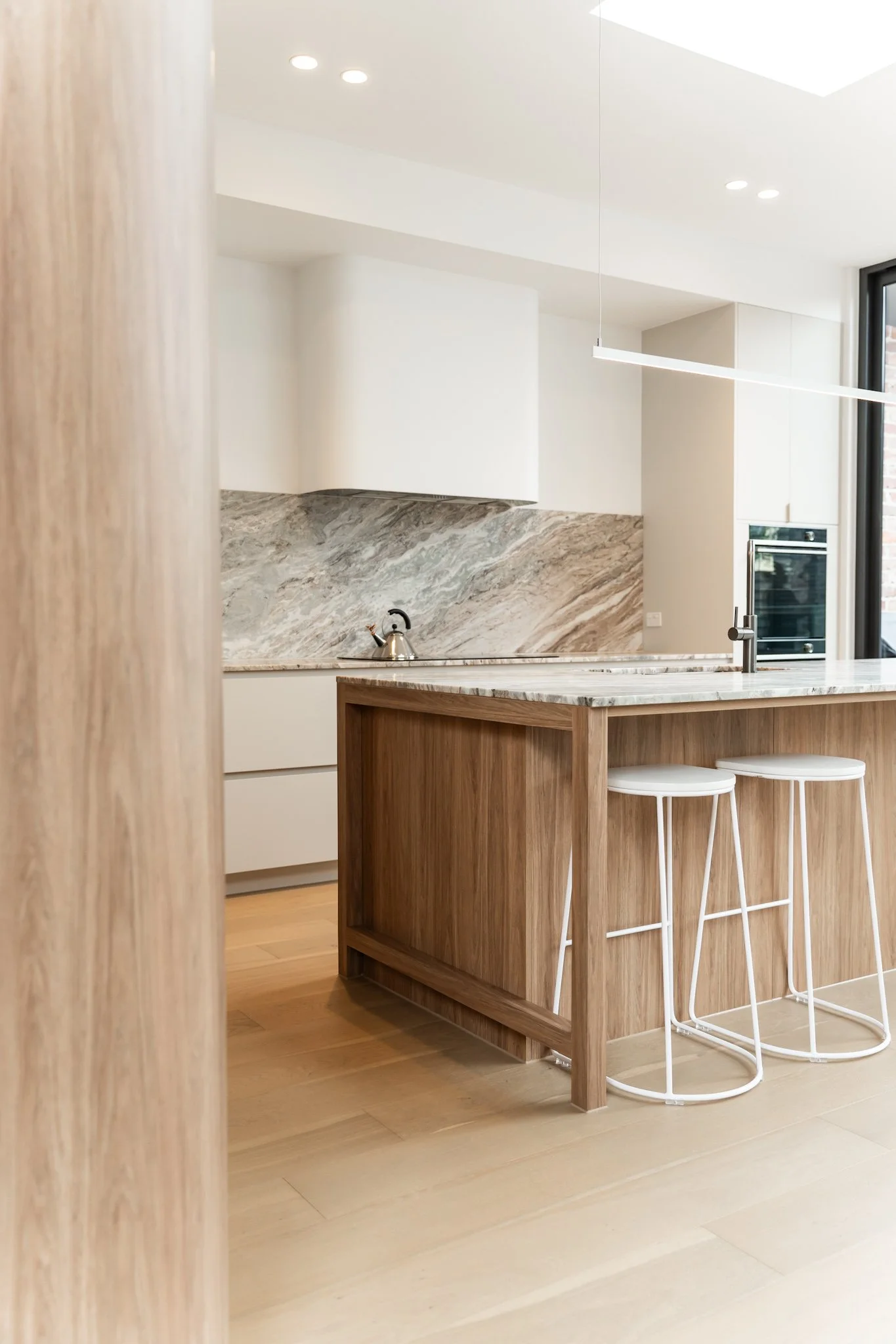 Modern kitchen with wooden island, marble countertop, white cabinets, and black window frame.