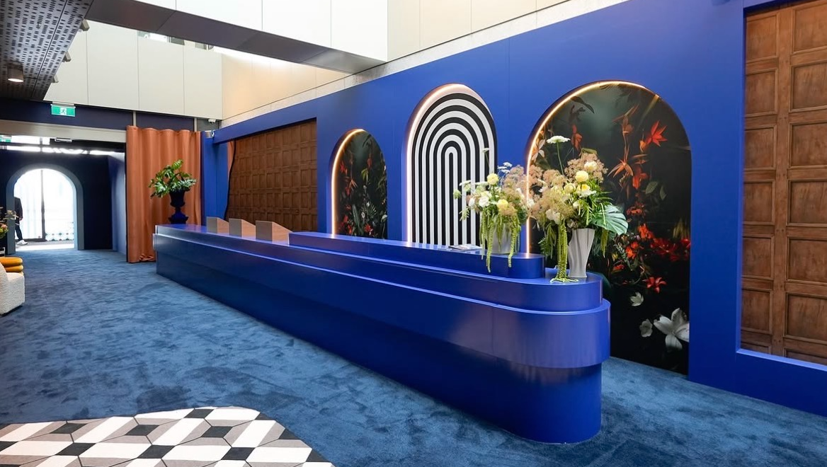 Modern interior with a blue reception desk, decorative arches, floral arrangements, and a patterned wall.