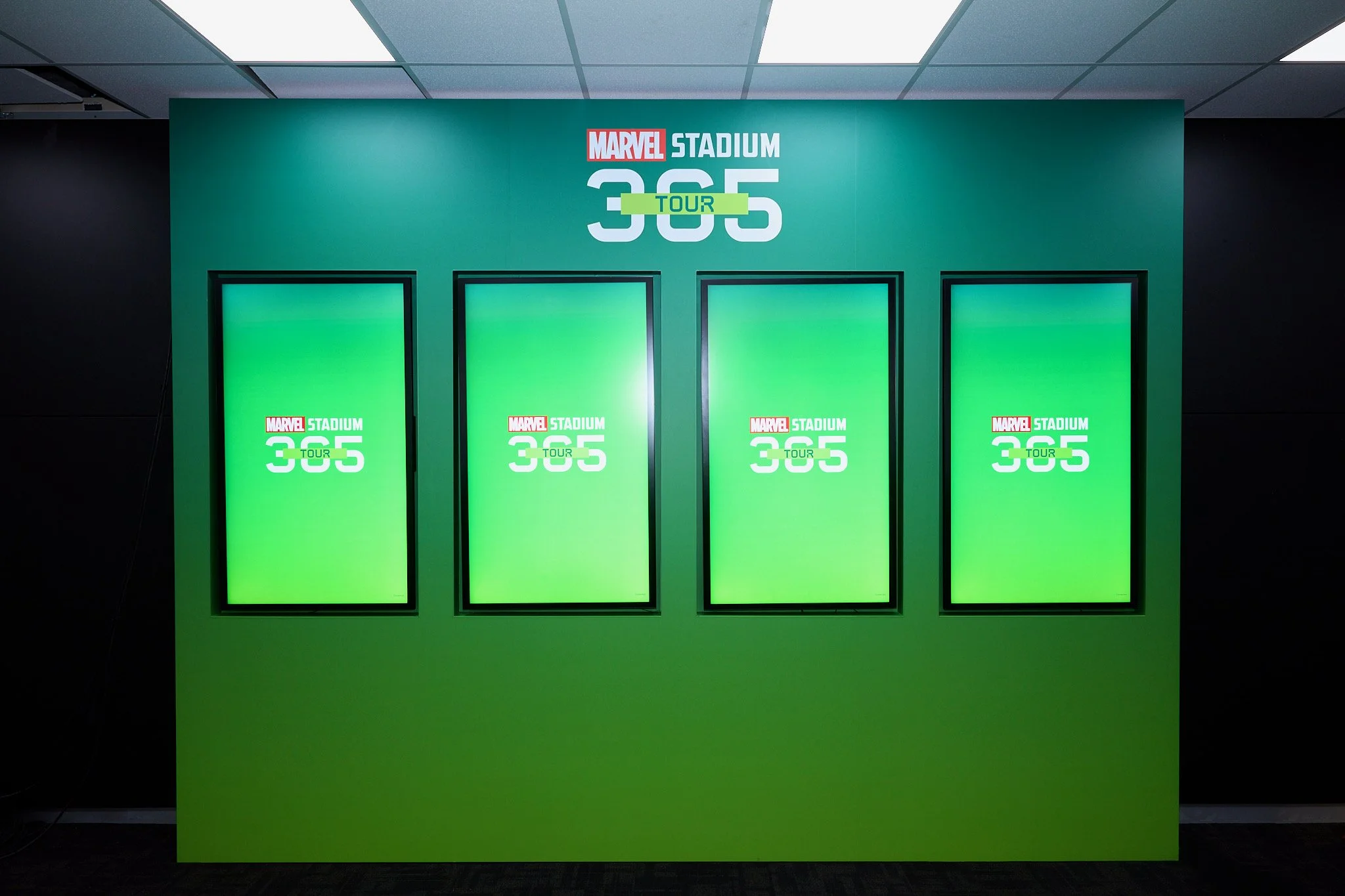 Green poster display with Marvel Stadium 365 TOUR logo and three blank digital screens.