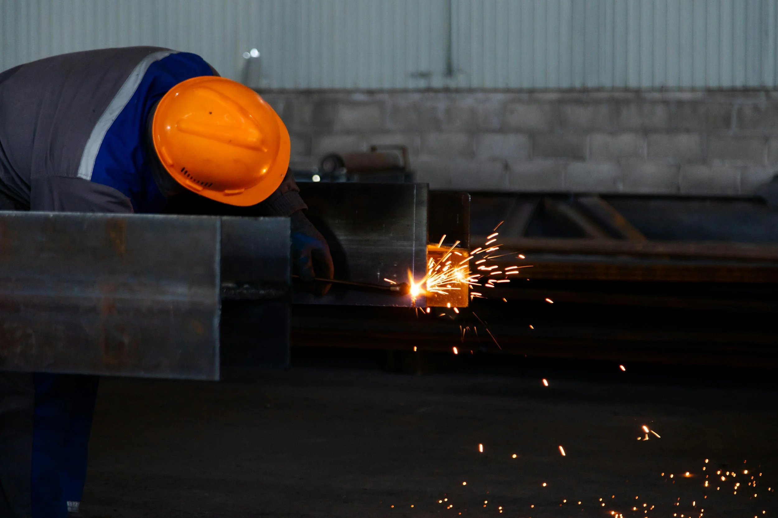 A worker in an orange safety helmet welding metal in an industrial workshop.