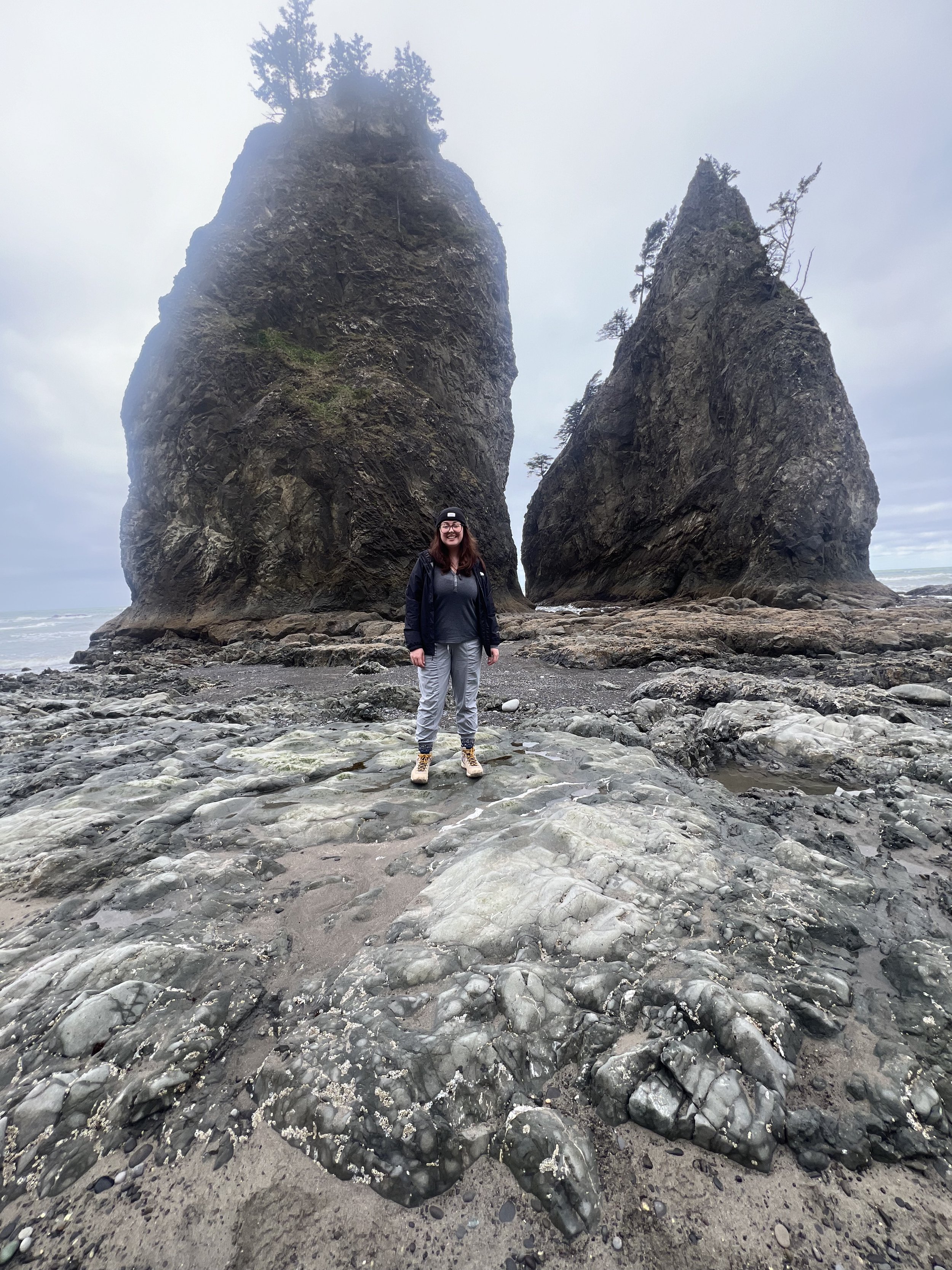 Caitie standing in front of a large rock on a stone beach