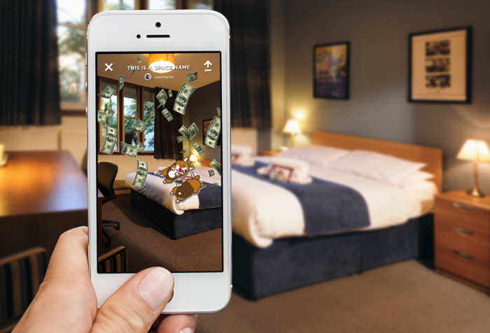 A person holding a smartphone displaying a photo of a hotel room with cartoon animals and flying dollar bills, with the actual hotel room in the background.
