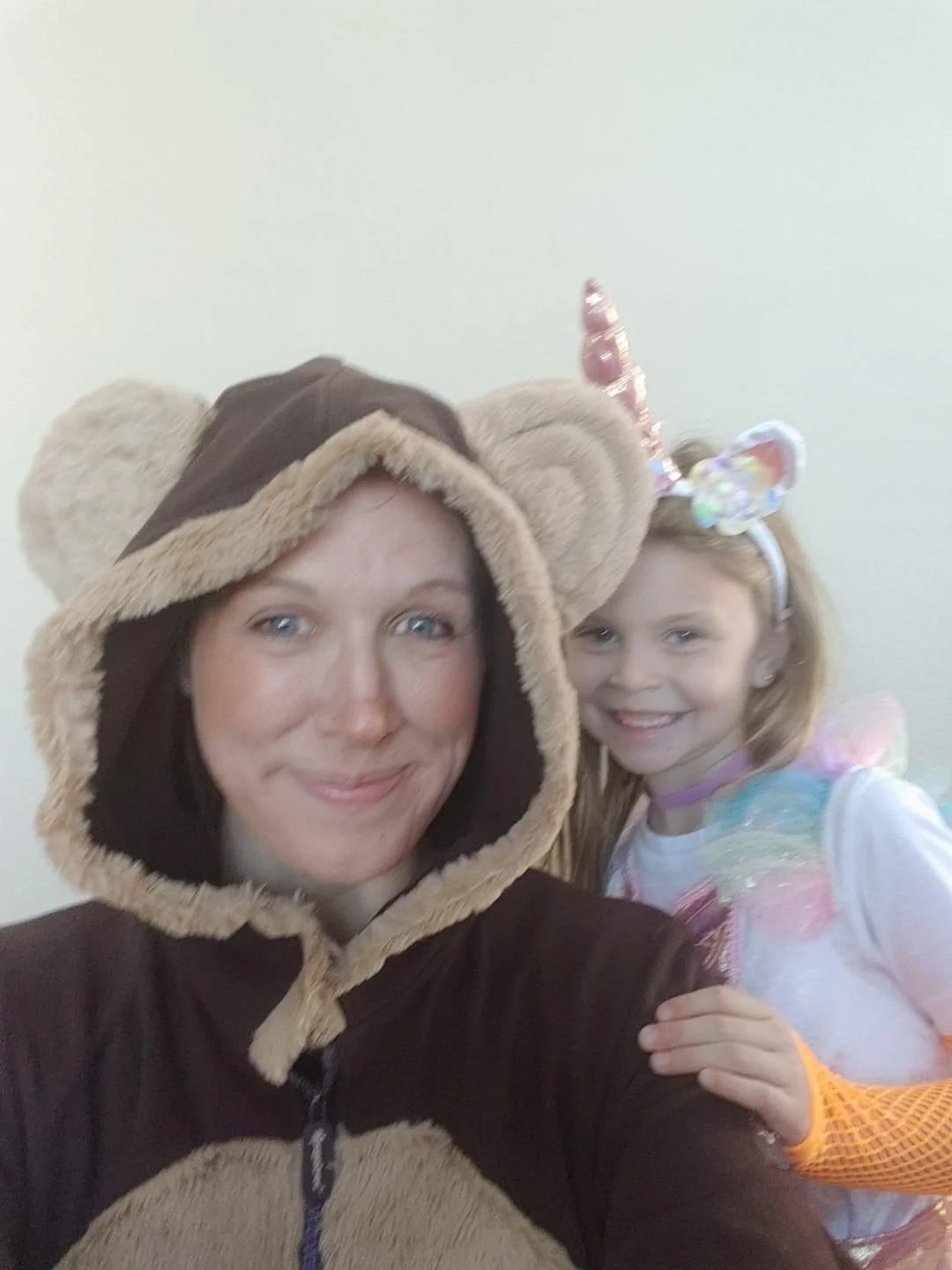 A woman dressed in a monkey costume and a young girl in a rainbow unicorn costume smiling together.