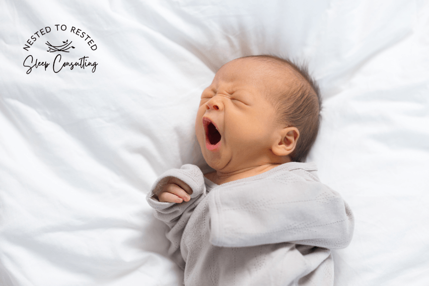 Sleepy newborn baby yawning in a white swaddle