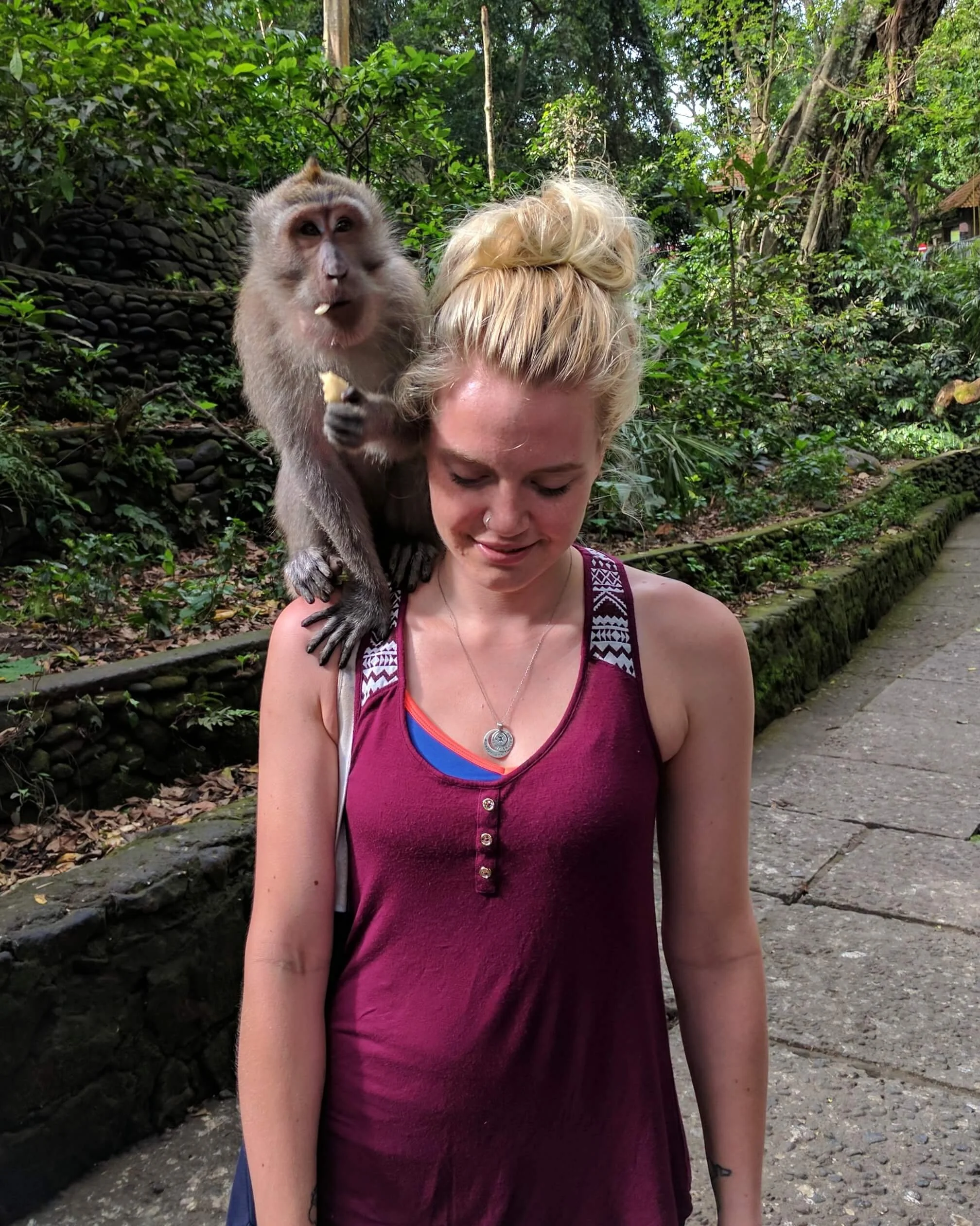Kyenna in the Monkey Forest in Ubud, Bali. There is a monkey on her left shoulder and it's eating a banana and looking in the camera.