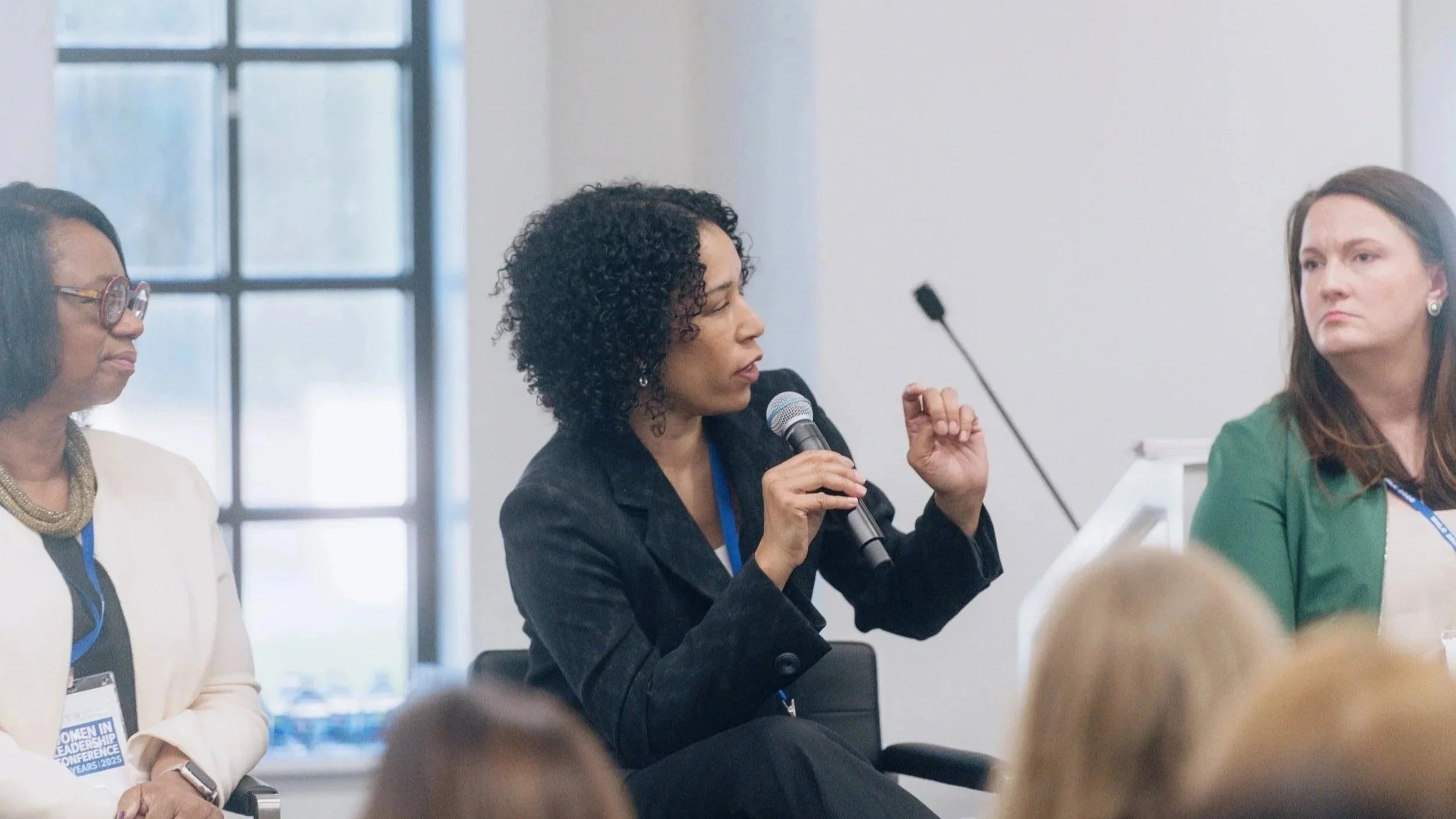 Three women sitting at a panel discussion with one woman speaking into a microphone.