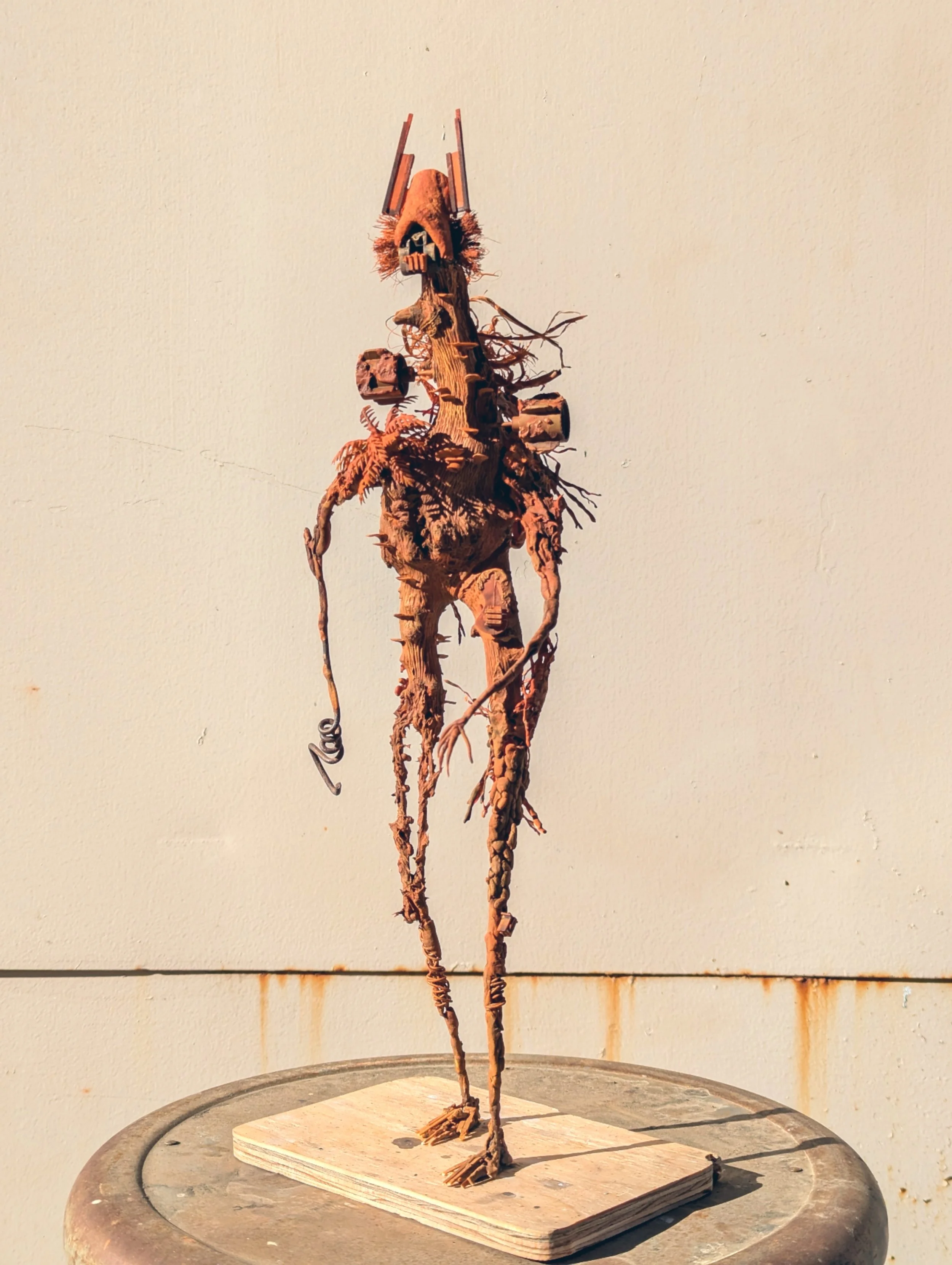 A tall, abstract sculpture resembling a humanoid figure made from twisted and carved wood, standing on a wooden base.