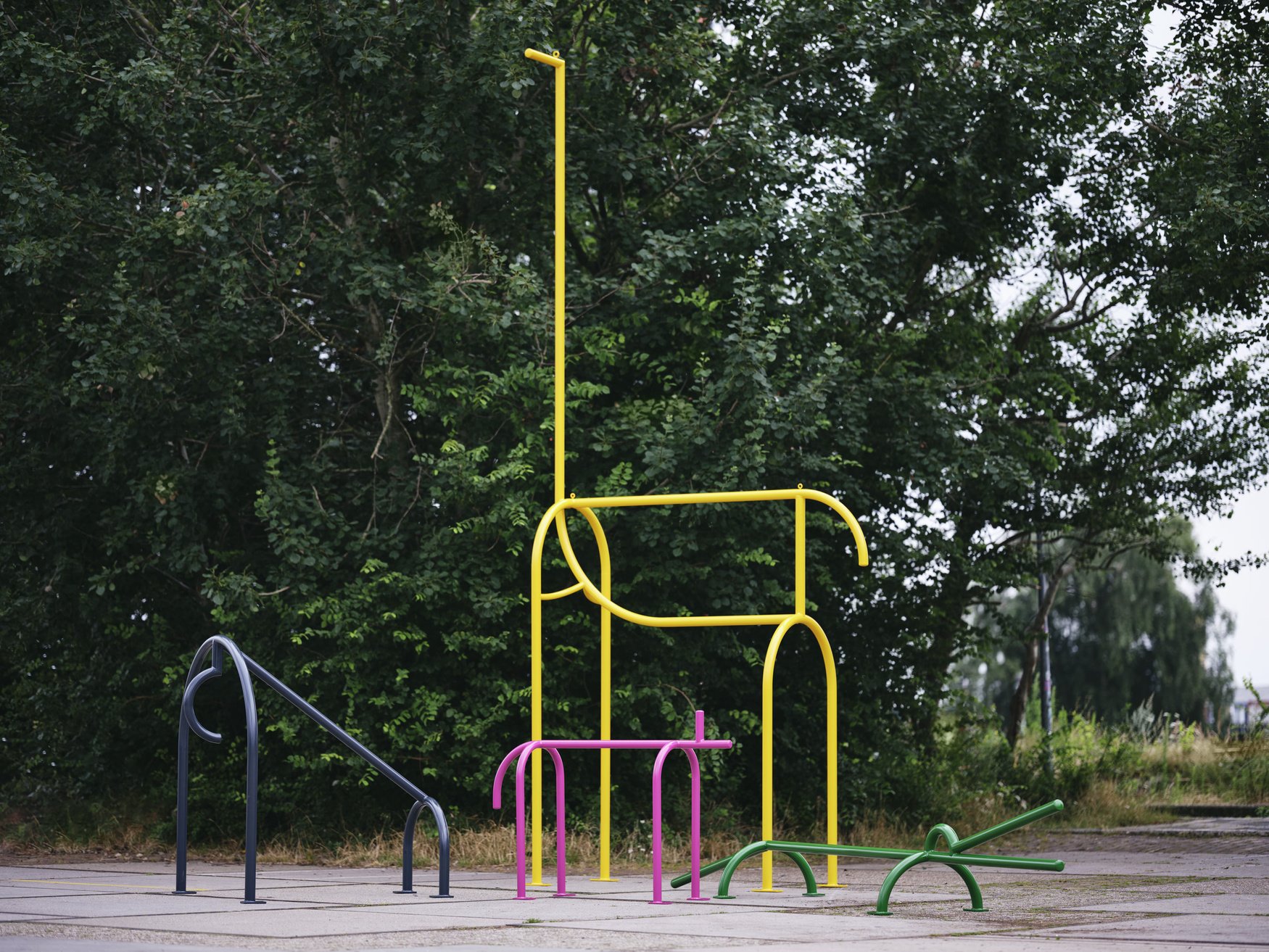 Colorful metal playground climbing structures and bars in an outdoor park with trees in the background.