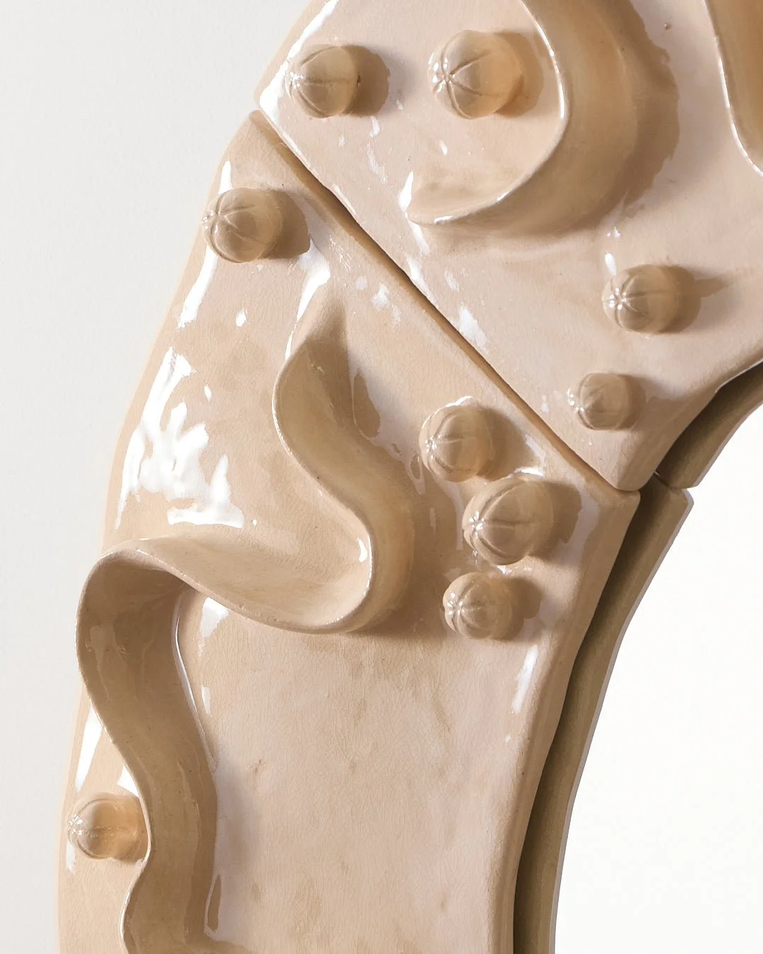 Détail du grand miroir rond en céramique. Pièce de décor modelé en terre blanche émaillé avec une couverte légèrement craquelée, avec des détails en relief ressemblant à des rubans ou des boulons.
