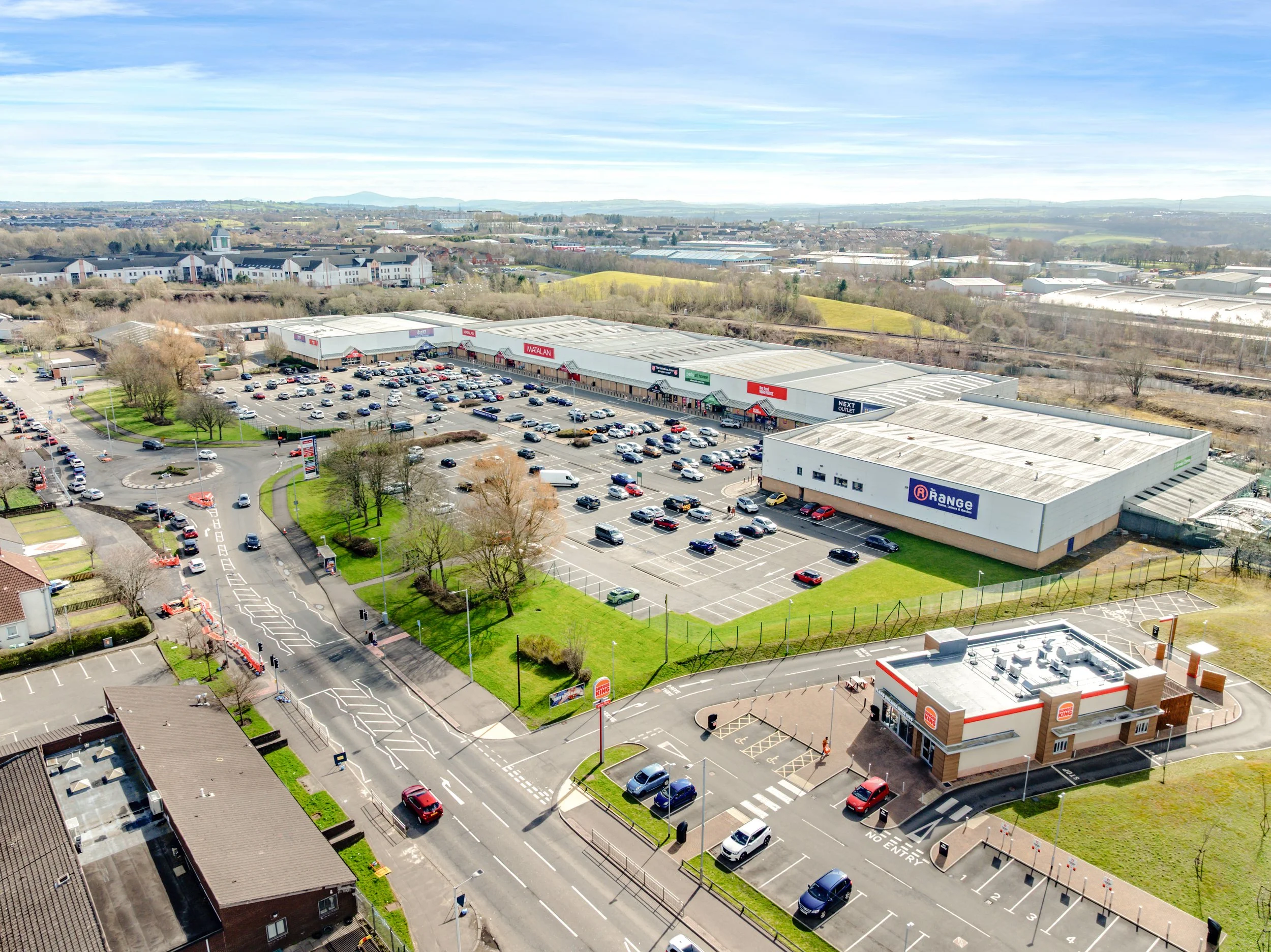 Retail warehouse building with a parking lot and cars in front, blue sky with clouds in the background.