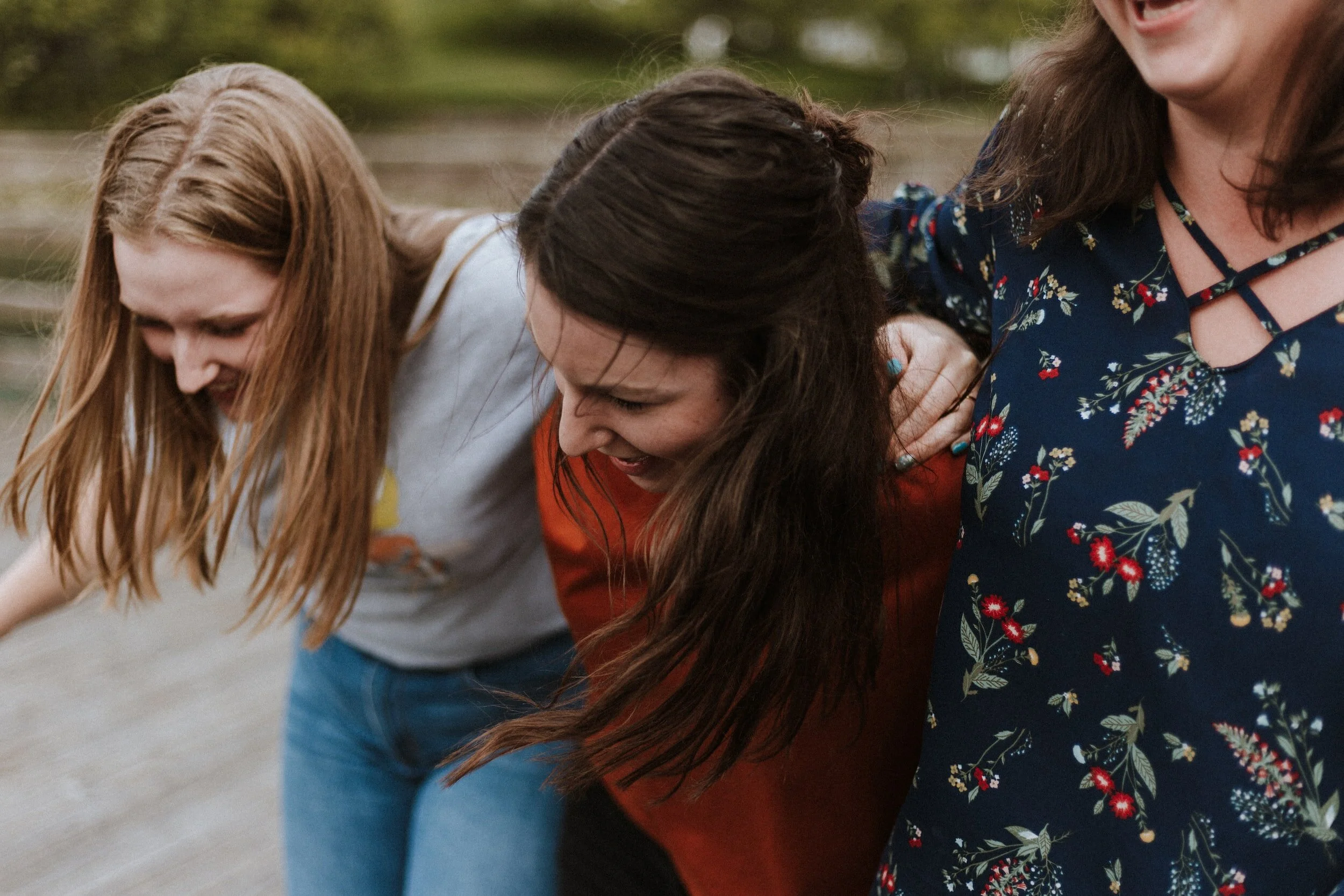 Three women laughing and embracing outdoors.
