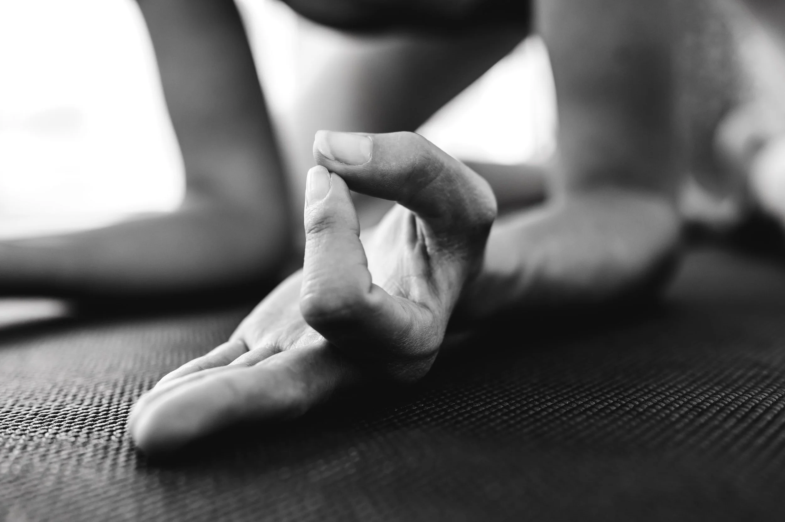 Close-up of a hand in a yoga mudra gesture on a yoga mat, black and white.