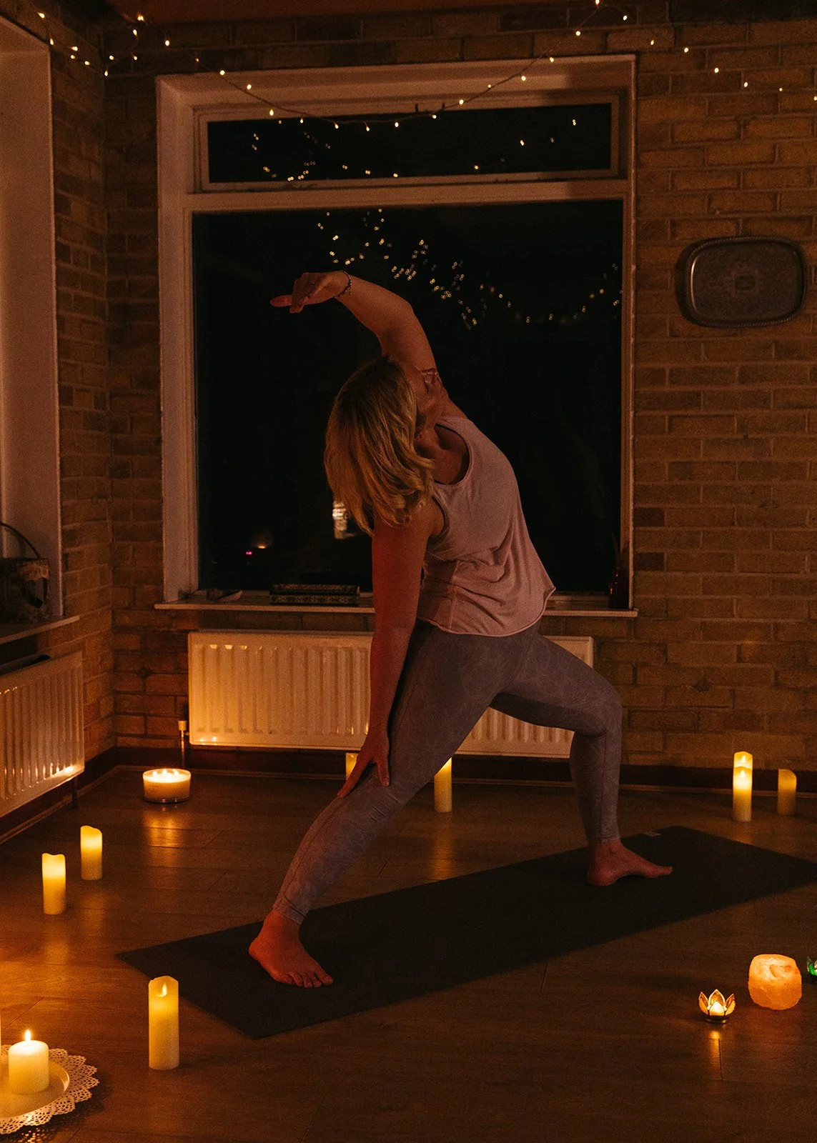 Person practicing yoga in a dimly lit room with candles and string lights.