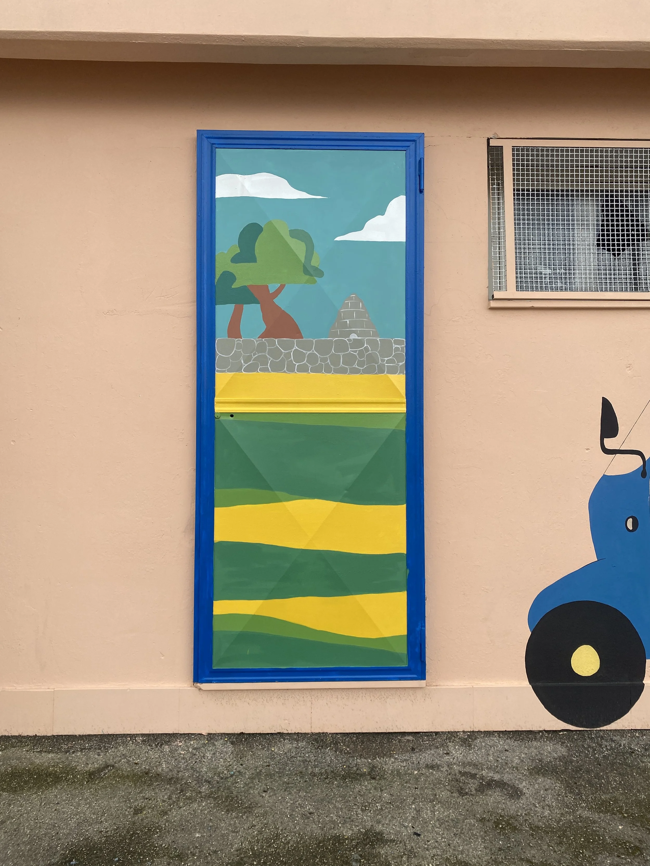Colorful mural depicting a landscape with trees, a stone wall, a conical structure, and fields with yellow and green strips, framed in blue on a pink wall.