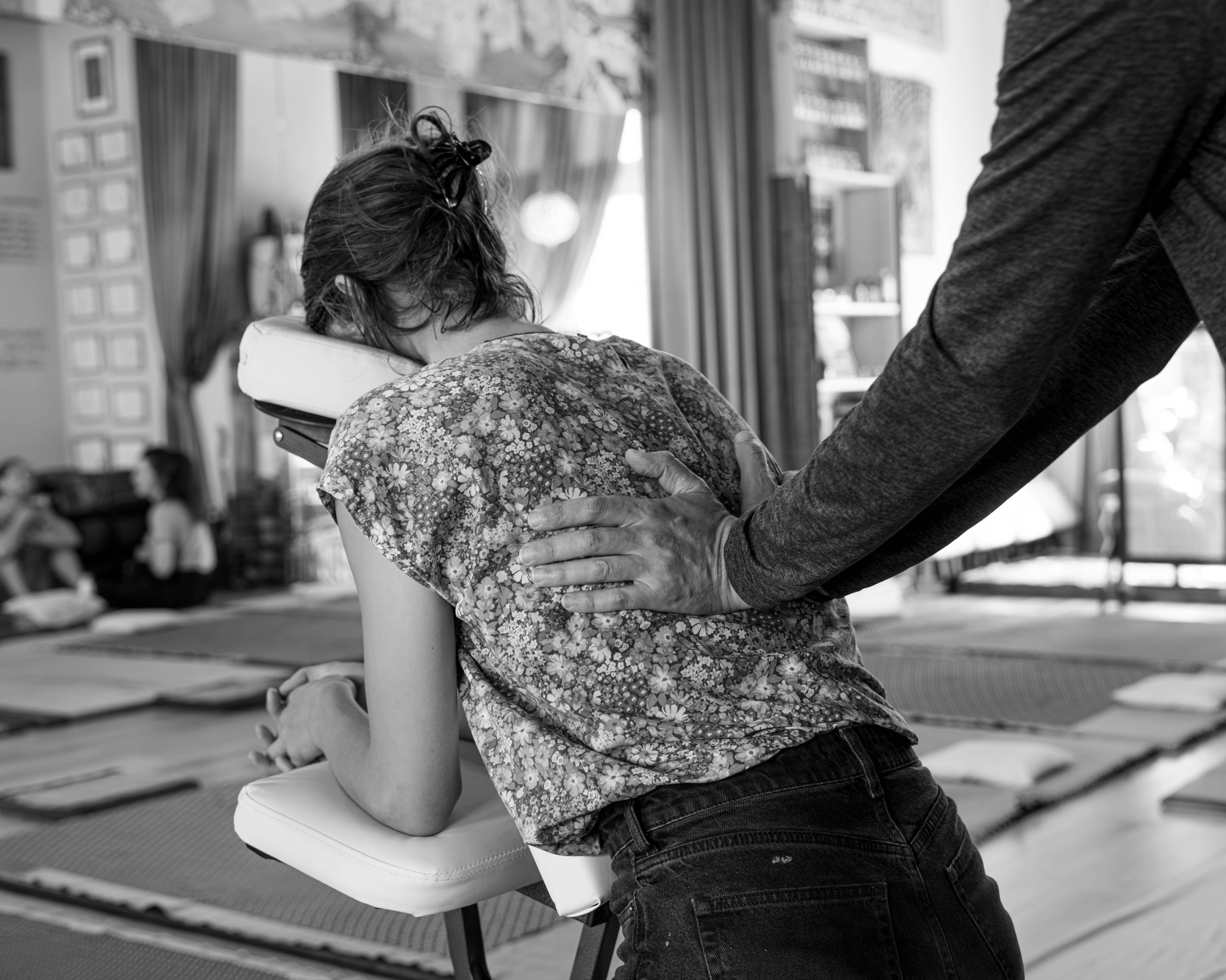 Person receiving seated back massage in relaxation setting, black and white.
