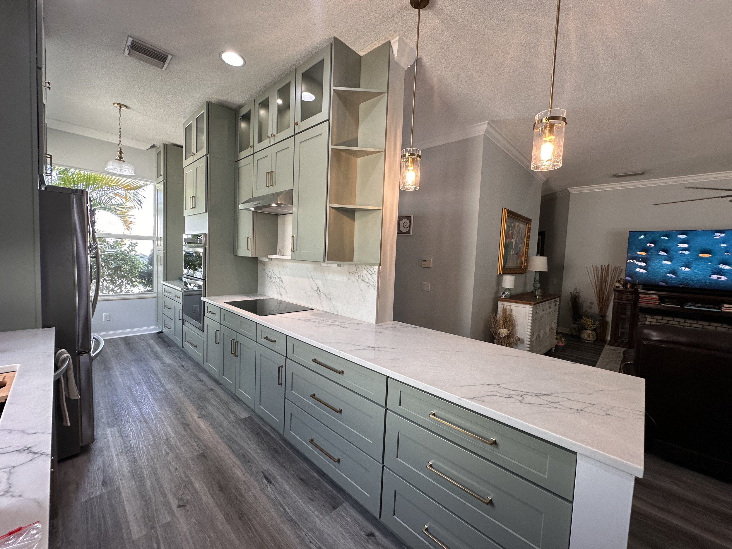 Modern kitchen with light green cabinets, white marble countertops, and pendant lights.