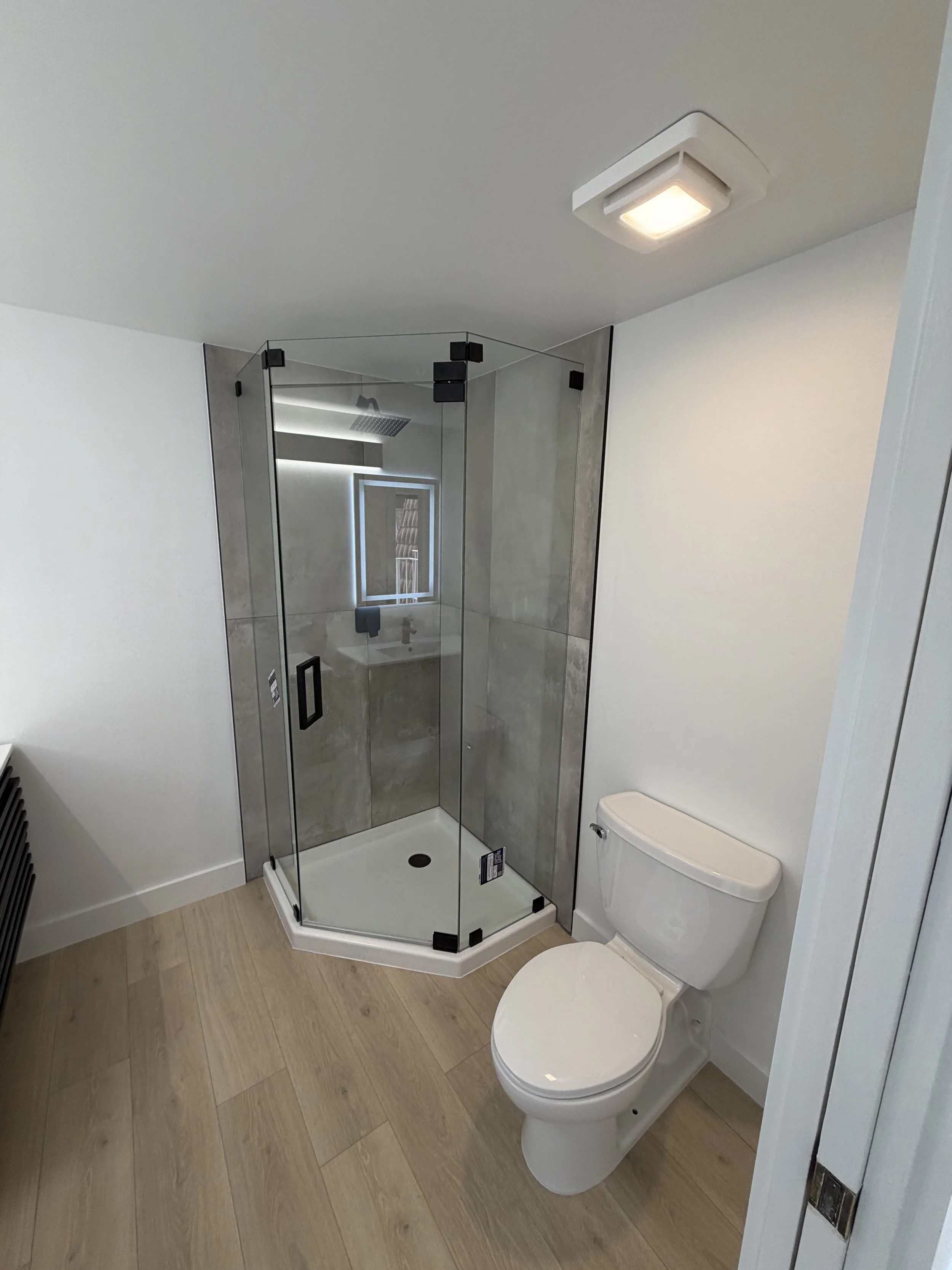 Modern bathroom with a glass shower enclosure, a toilet, and light wood flooring.