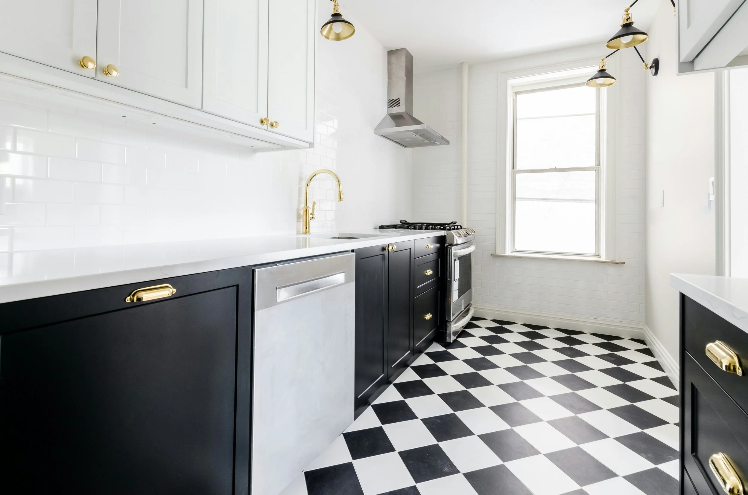 A modern kitchen with black and white cabinets, a yellow faucet, a stainless steel stove, and black and white checkered flooring.