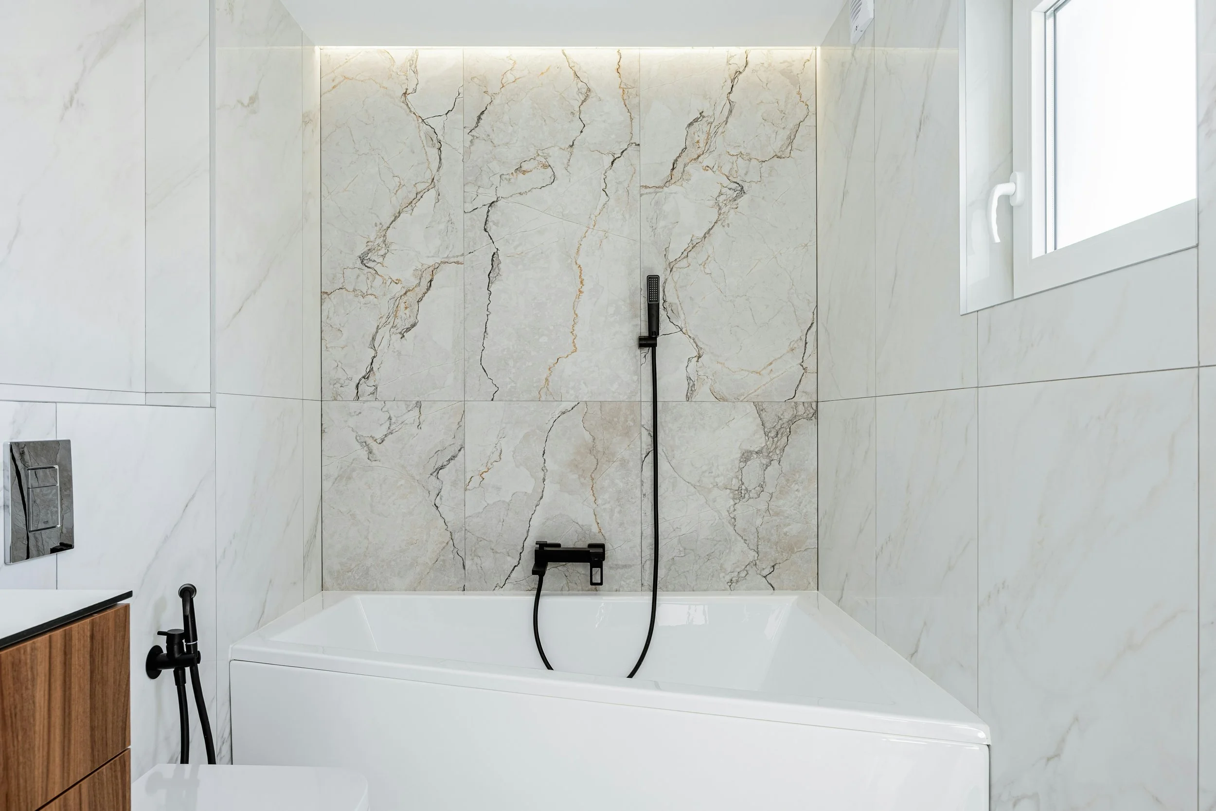 Modern bathroom with marble walls, black shower fixtures, a window, and a bathtub.