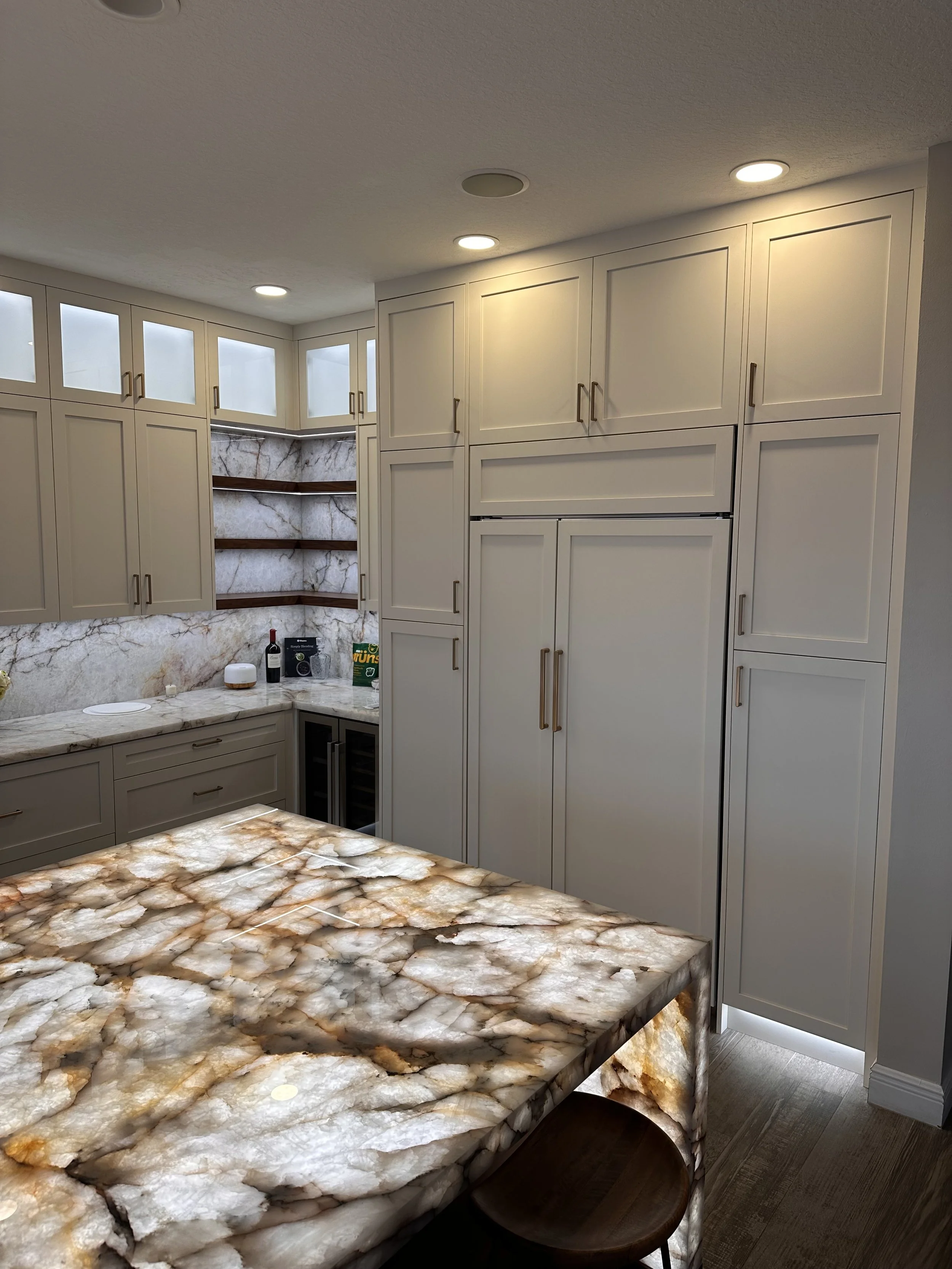 A kitchen with white cabinets, a marble backsplash, and a marble countertop and island with a brownish-orange pattern.