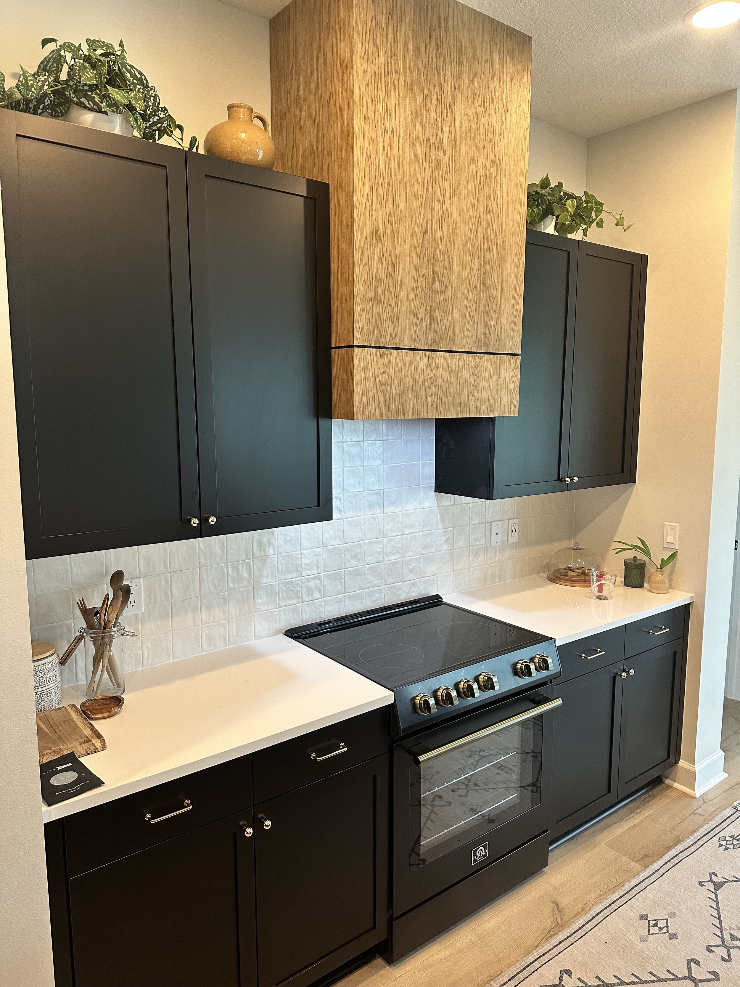 A modern kitchen with black cabinets, a white countertop, a black stove, and decorative plants and vases on top of the cabinets.