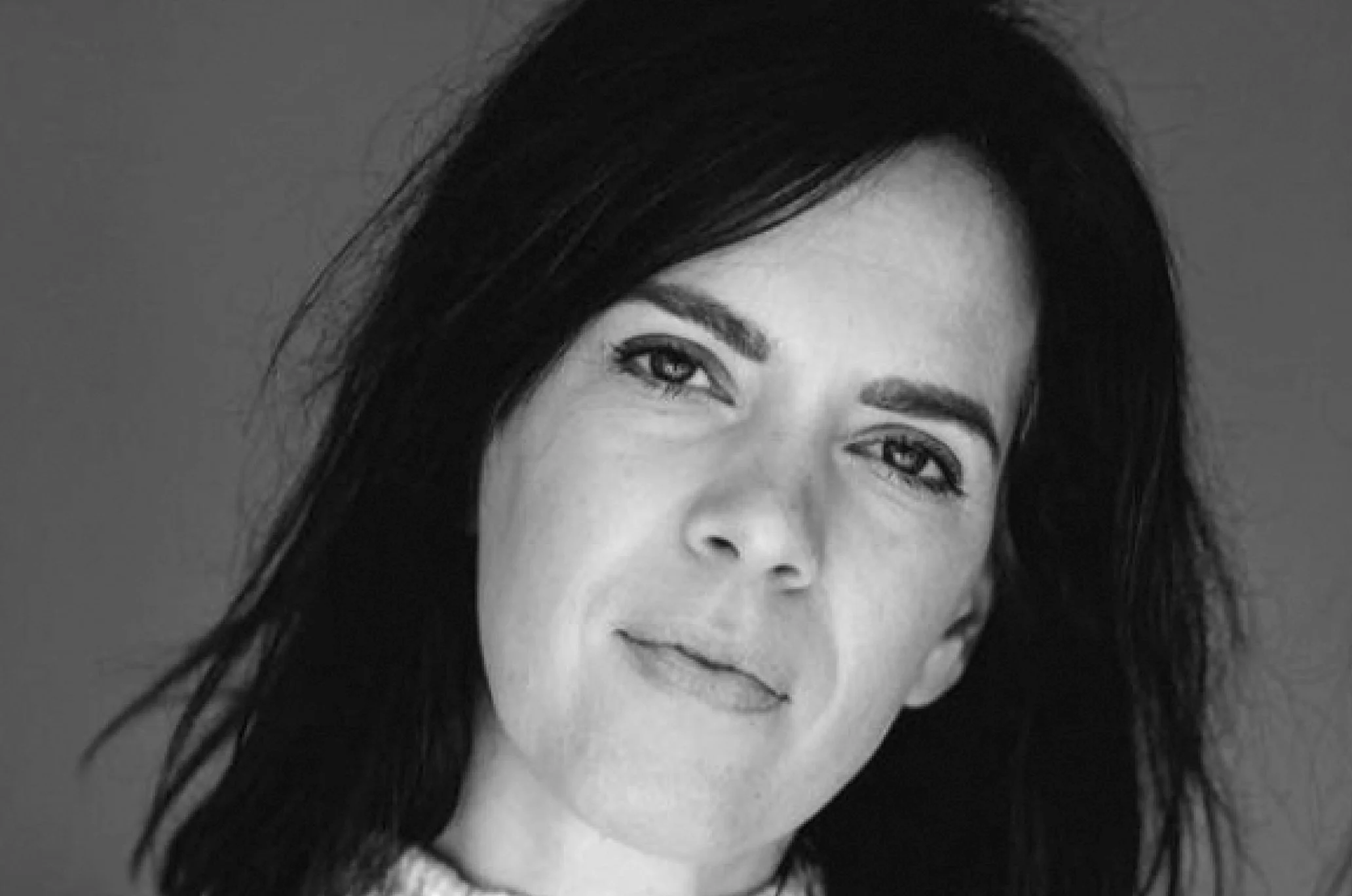Black and white portrait of a woman with dark hair, looking at the camera with a neutral expression against a plain background.
