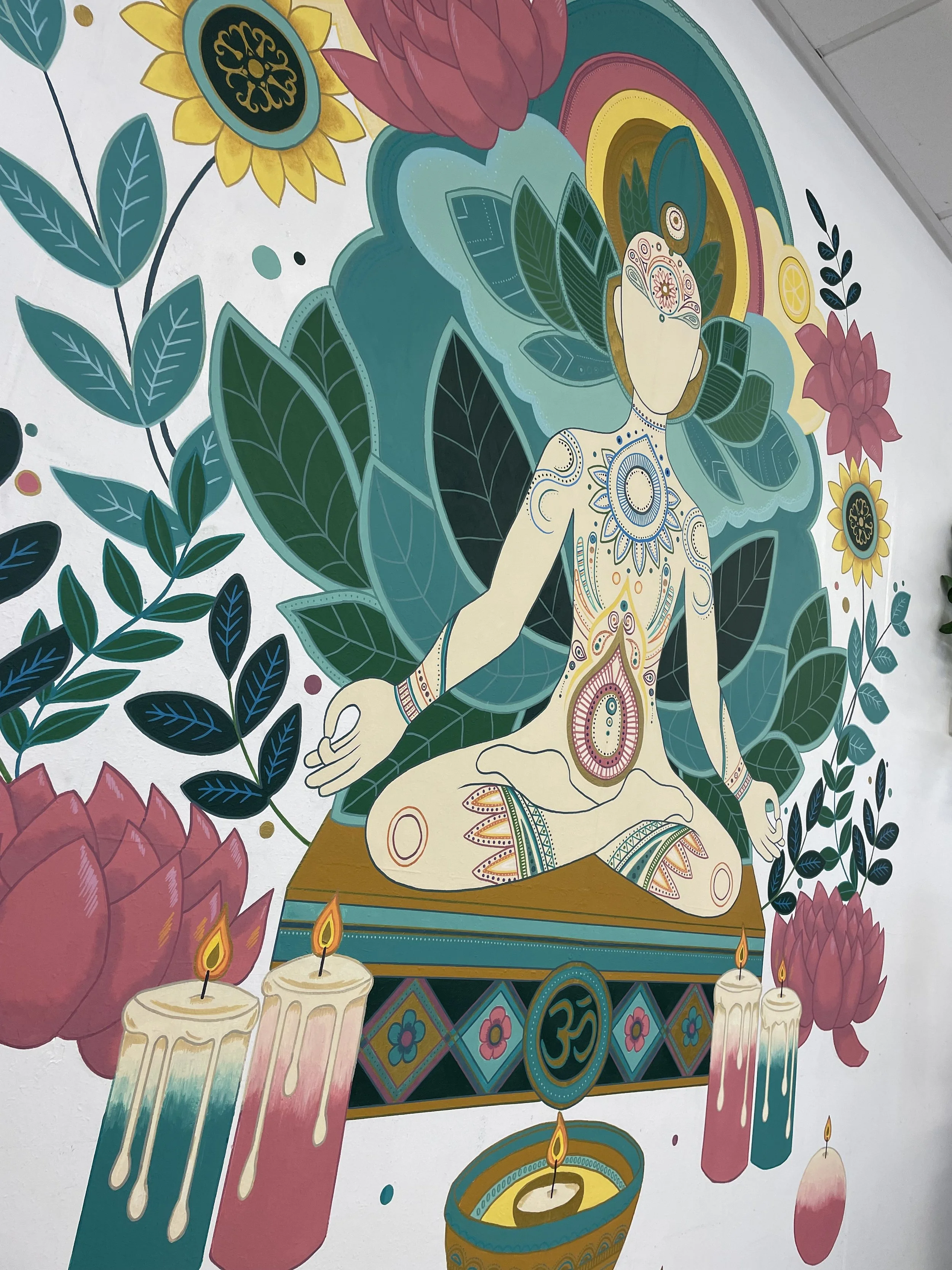 Colorful mural depicting a meditative figure surrounded by large green leaves, vibrant flowers, and lit candles, with a decorative background.