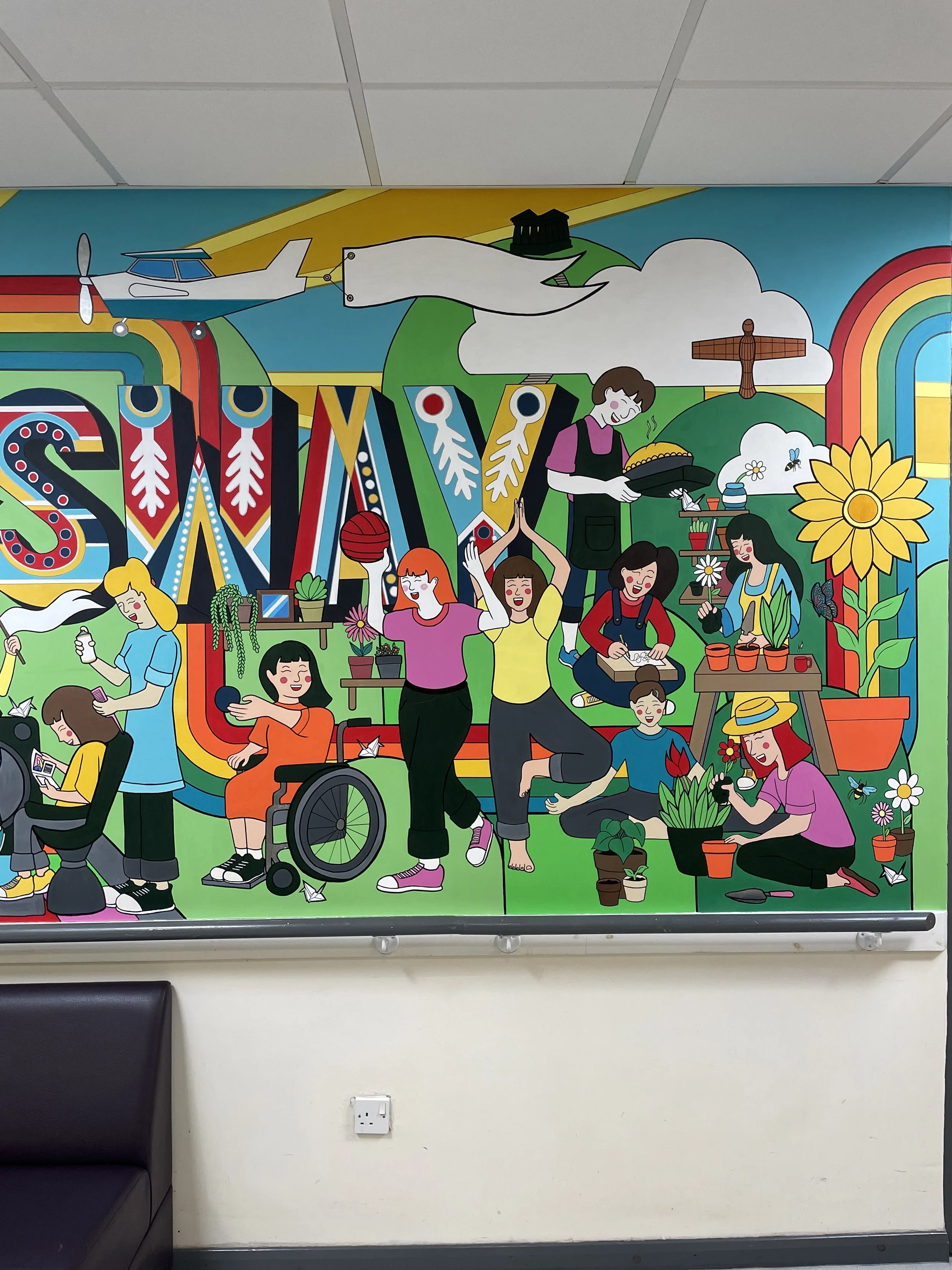 Colorful mural illustrating a community gardening scene with women planting and tending flowers, a person in a wheelchair, a woman holding a spray bottle, and a person watering plants. The mural features a large sunflower, rainbows, clouds, a bird, a