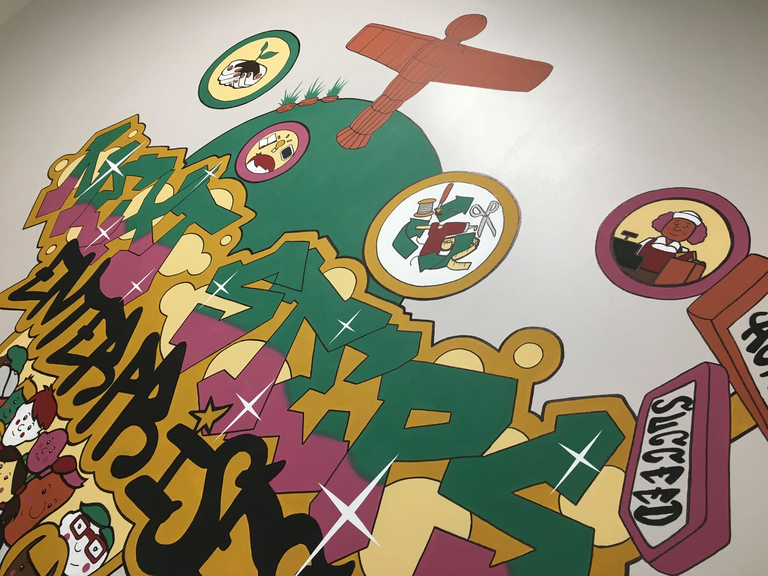 Colorful mural with a green globe featuring various cartoon characters and icons, including a person working at a cash register, a woman with glasses reading a book, a person with a beaker, and a vintage plane, along with large 3D text and a sign rea