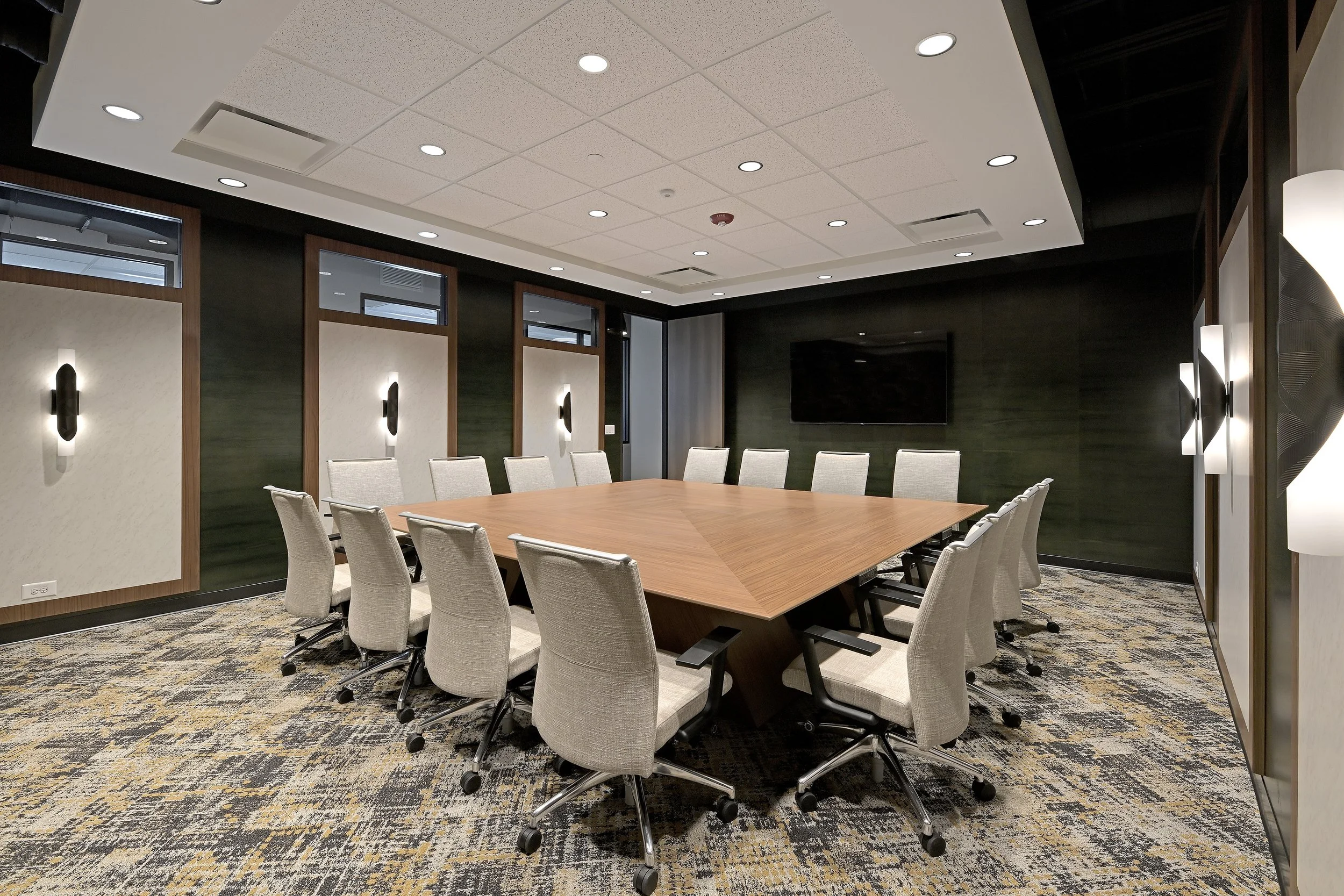 Custom square conference table with fabric chairs. Dark green wallpaper accents.