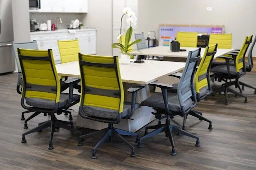 Light driftwood finish square conference tables with neon yellow and gray chairs