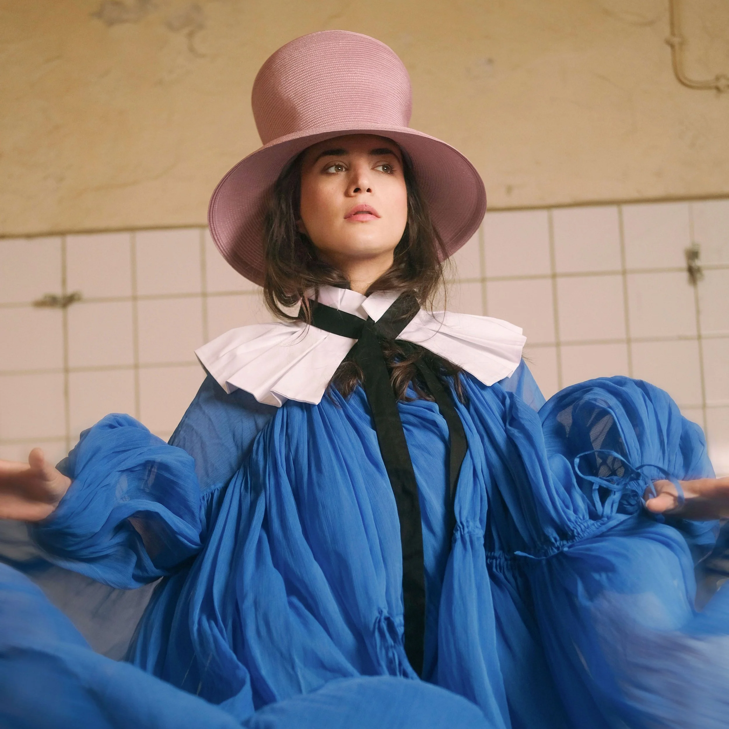 Künstlerin Dënalisa Shijaku in einem blauen Kleid und auffälligem Hut