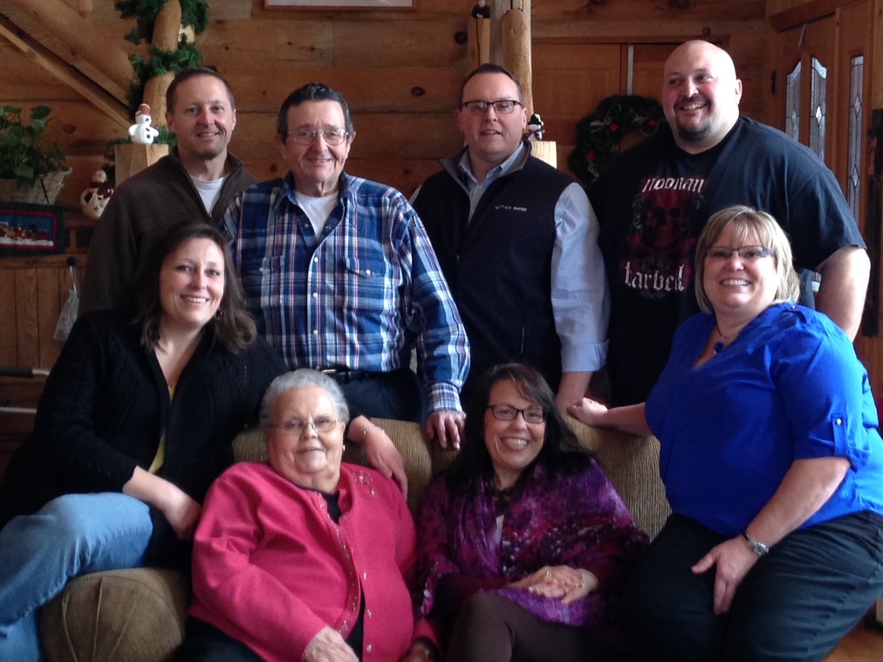 A group of eight people posing indoors with wooden walls and Christmas decorations.