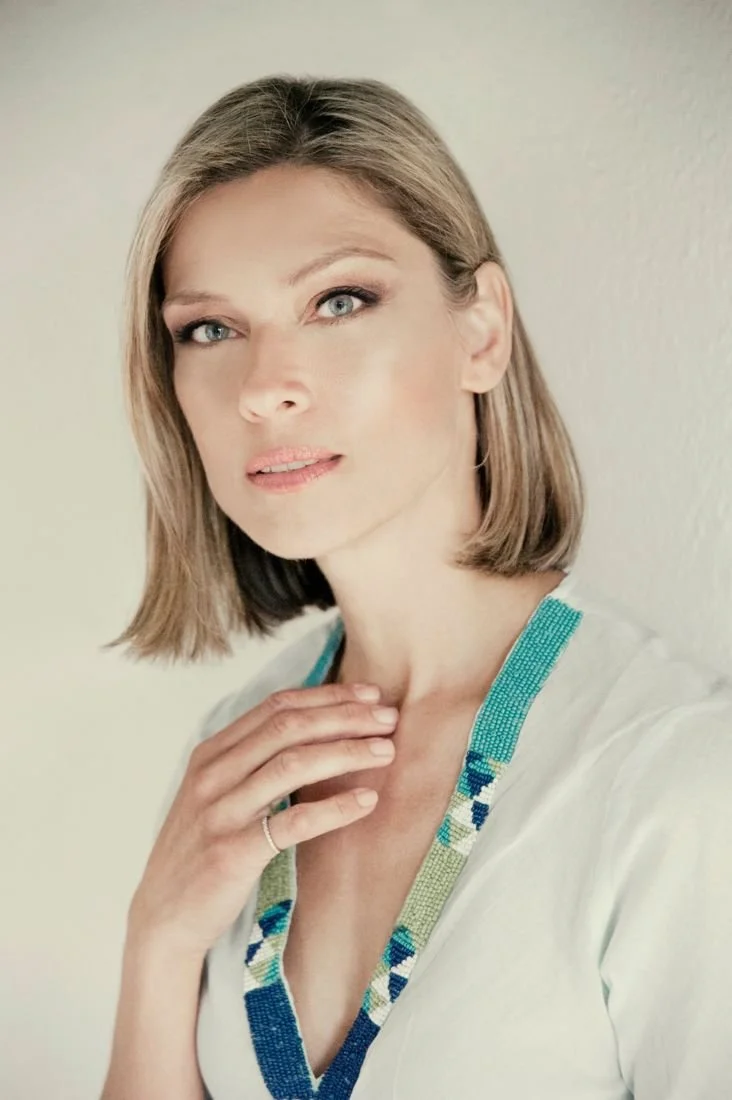 Woman with a short bob and a turquoise beaded necklace, hand at her collarbone