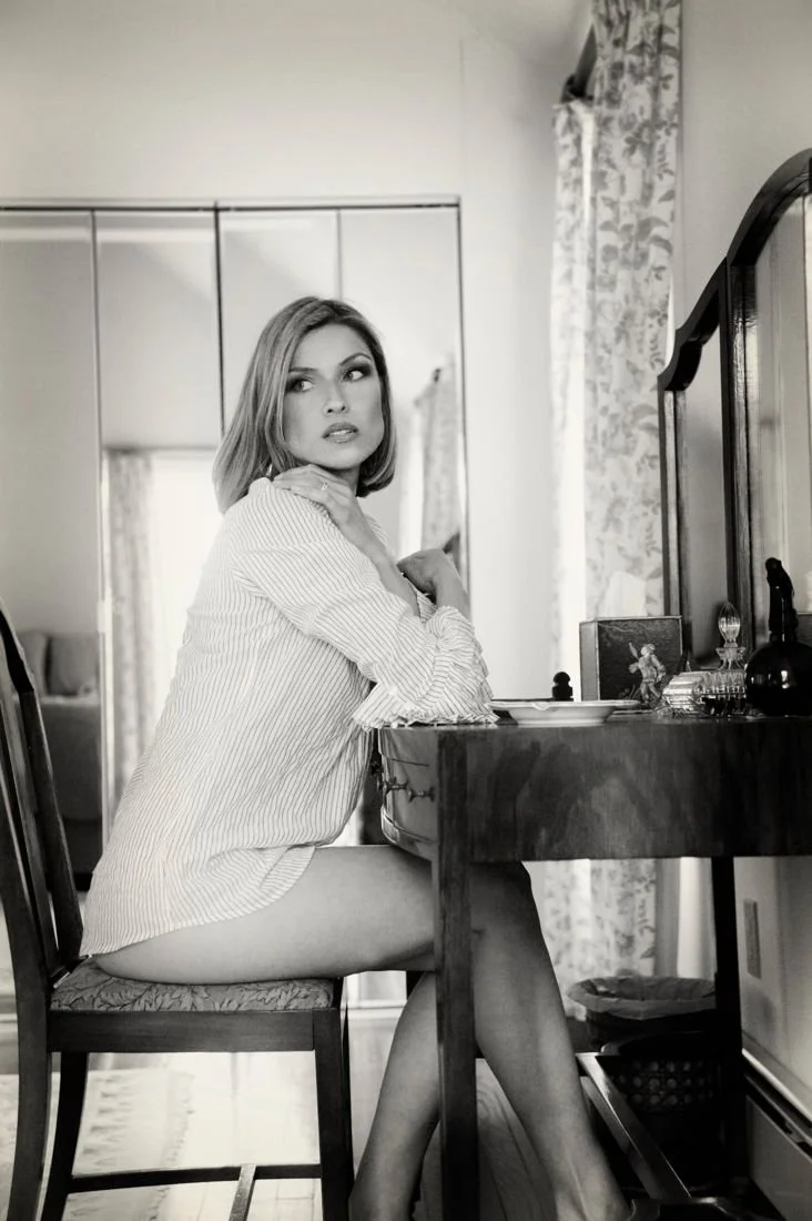 Black and white photo of a woman in a white shirt seated at a vanity
