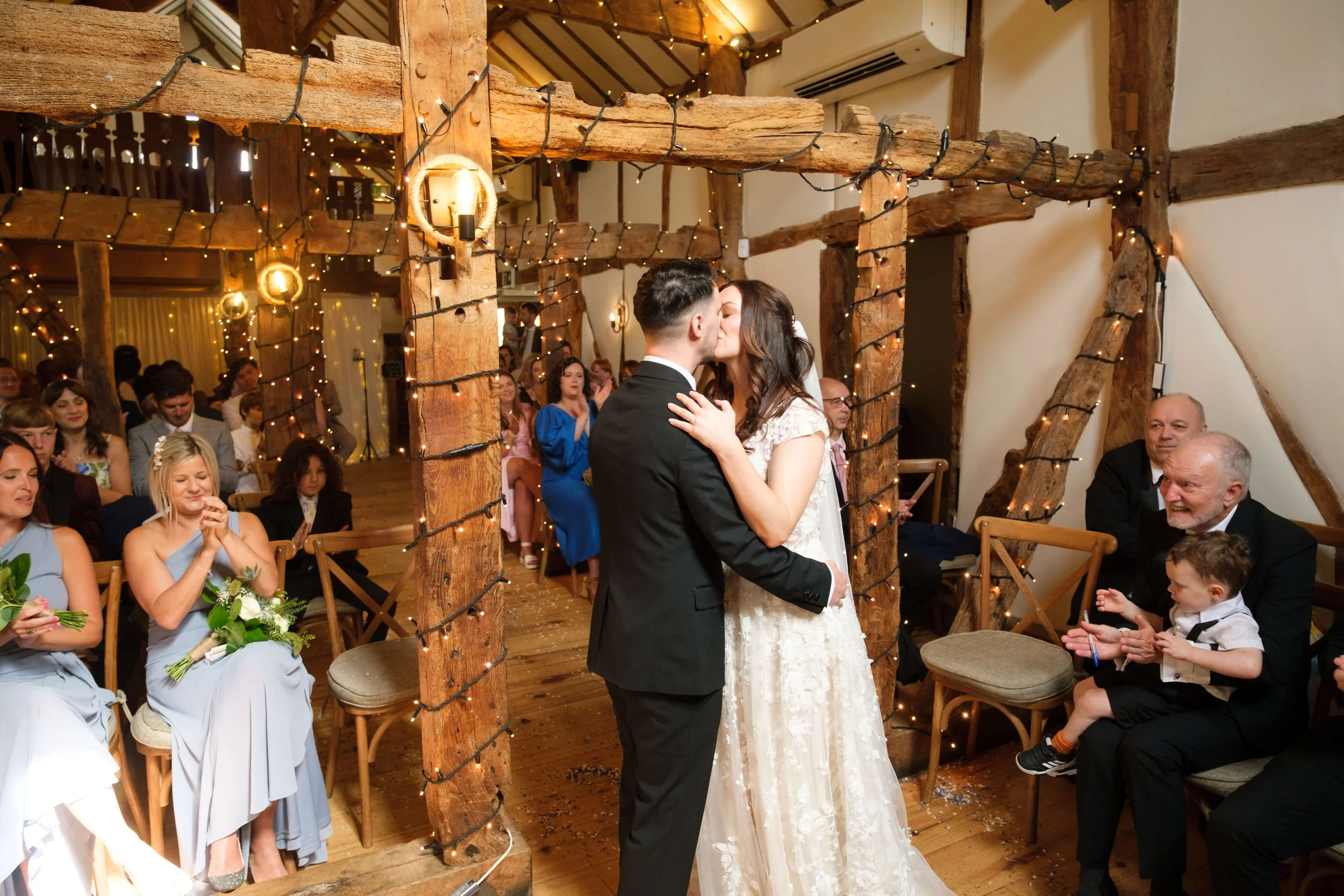 Wedding at the Plough Inn, Eaton. Bride and Groom sharer their first kiss in front of the family in the historic barn