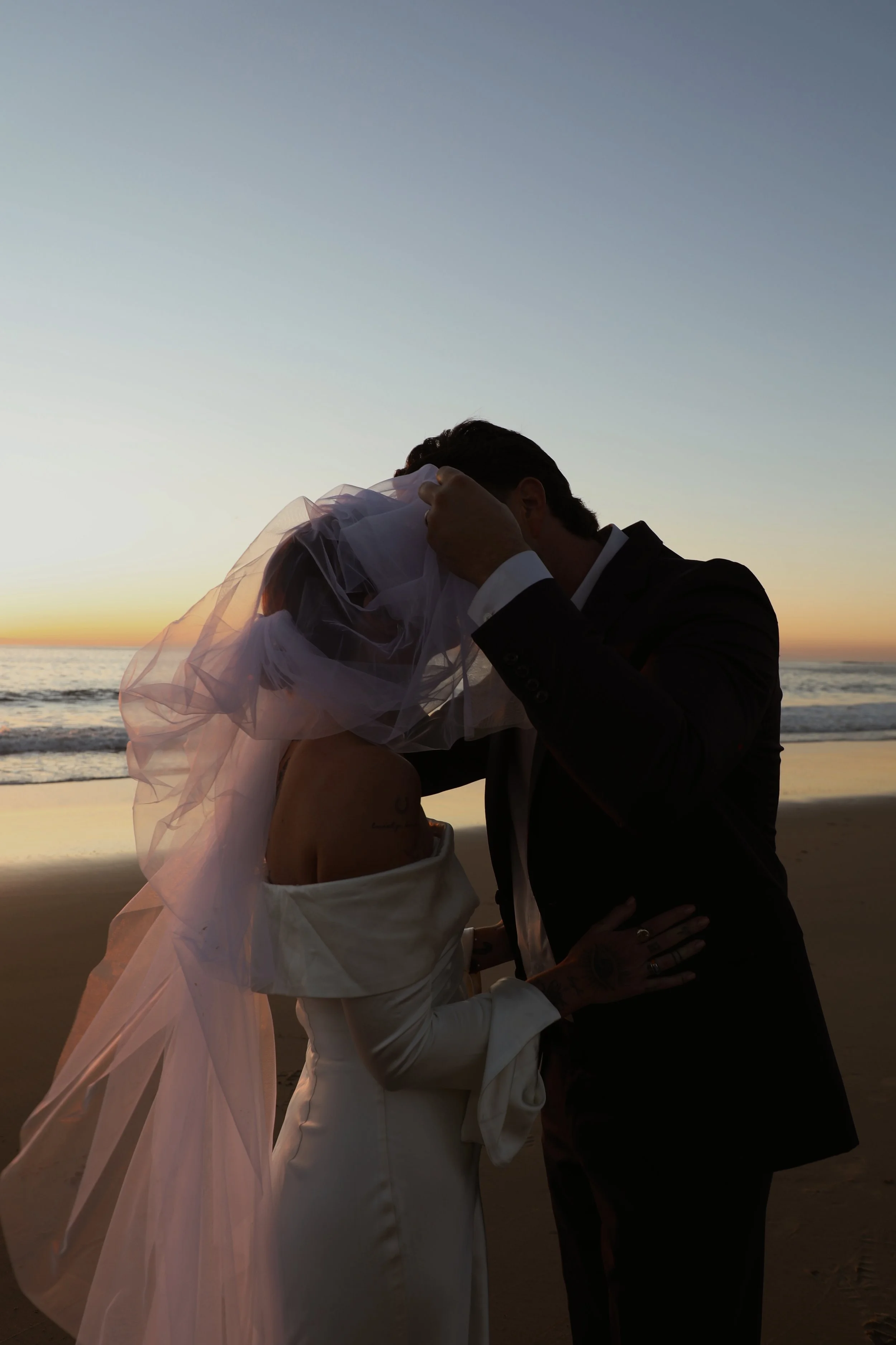 A couple dressed in wedding attire sharing an intimate moment at the beach during sunset