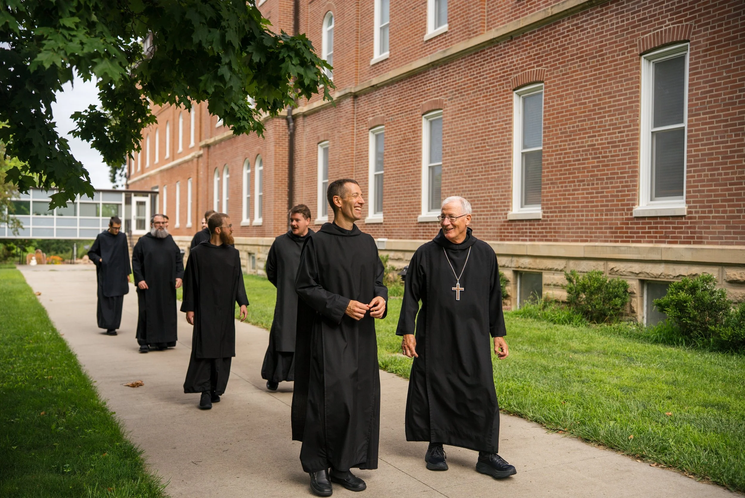 monks wearing black habits walking and laughing in front of brick building