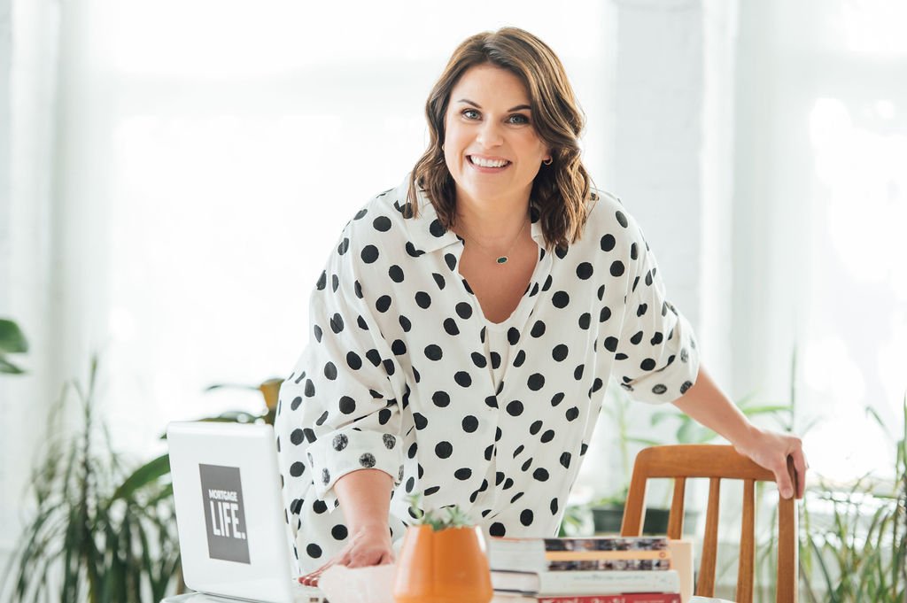 A businesswoman in a polka dot shirt poses for a personal branding photoshoot at a table with a laptop