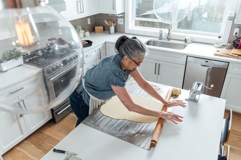 During a personal branding photoshoot, a woman in STEFANIA’S KITCHEN - PORTLAND, OR artfully rolls out dough in a kitchen