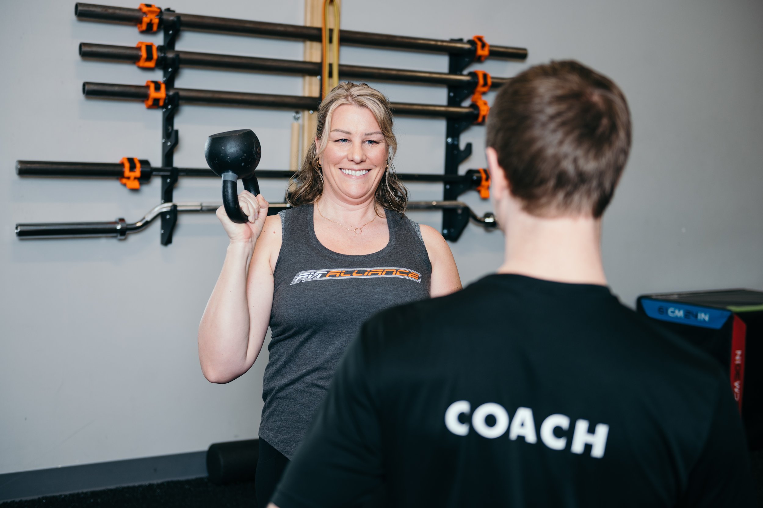 A woman holds a dumbbell in front of a couch from FIT ALLIANCE.