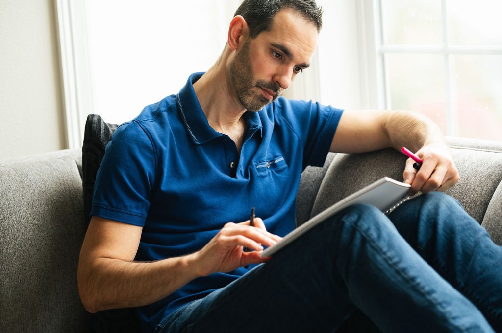 A professional branding photographer captures an individual sitting on a couch, engrossed in writing on a notepad