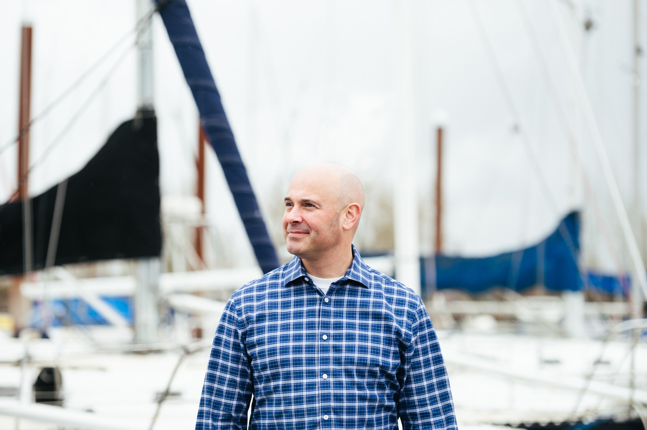 A man standing in front of a boat with sailboats. Captured in brand photography in Portland